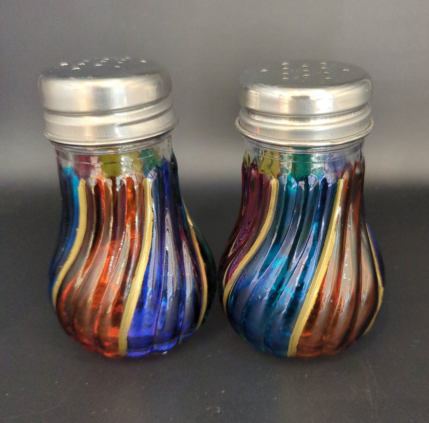 Colorful glass salt and pepper shakers on a dark surface