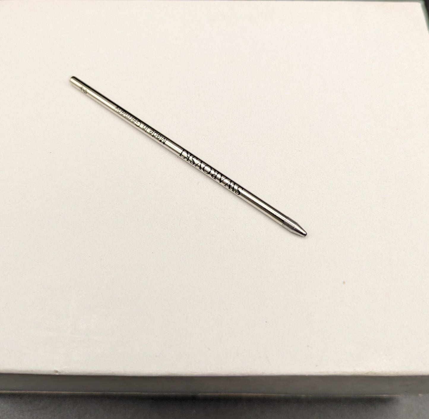 Metallic pen refill on a white surface with a black background