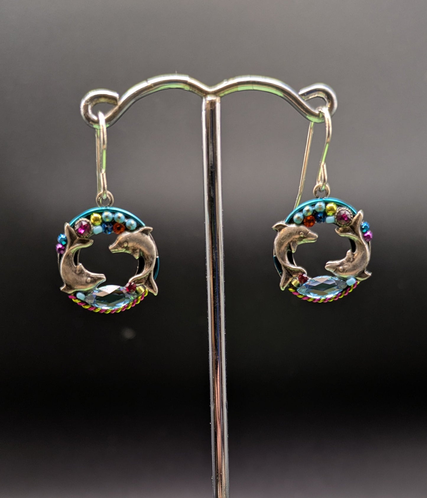 Dolphin-shaped earrings on a stand with a dark background