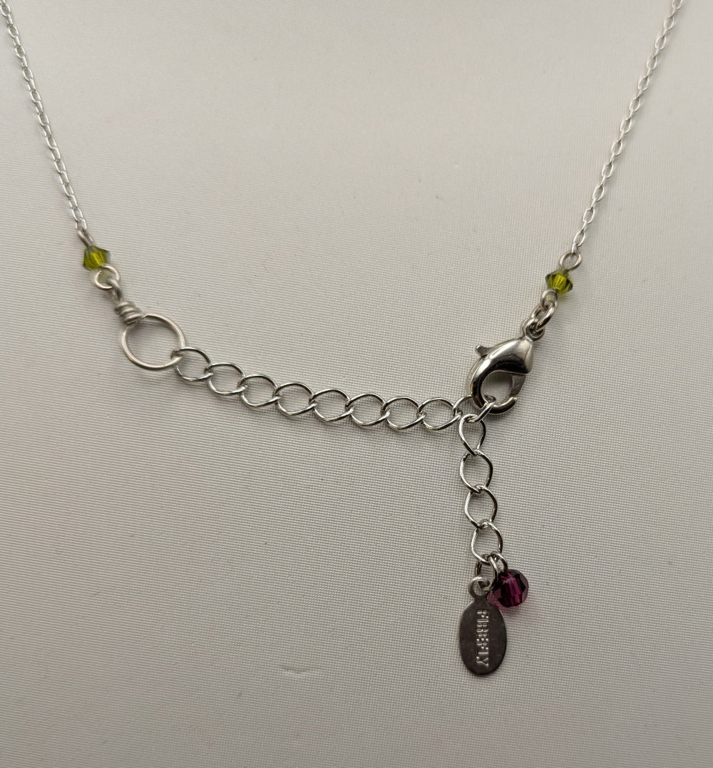 A silver chain necklace displayed on a white mannequin bust, featuring a lobster clasp, an adjustable link chain extender, and a small dangling oval charm with a dark red bead accent.