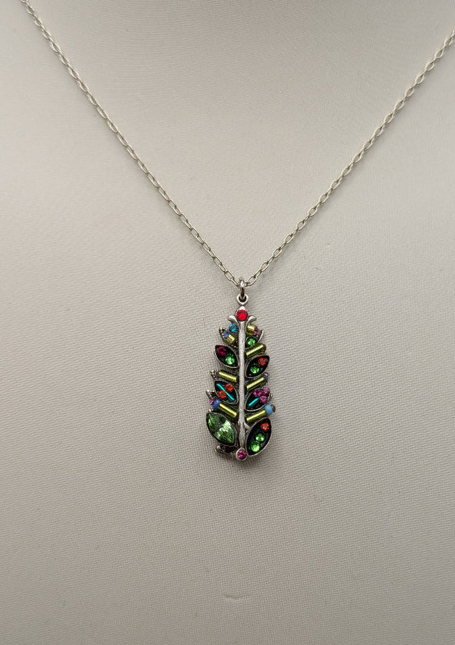 A silver chain necklace with a leaf-shaped pendant featuring iridescent multicolor rhinestones, displayed on a white mannequin bust.