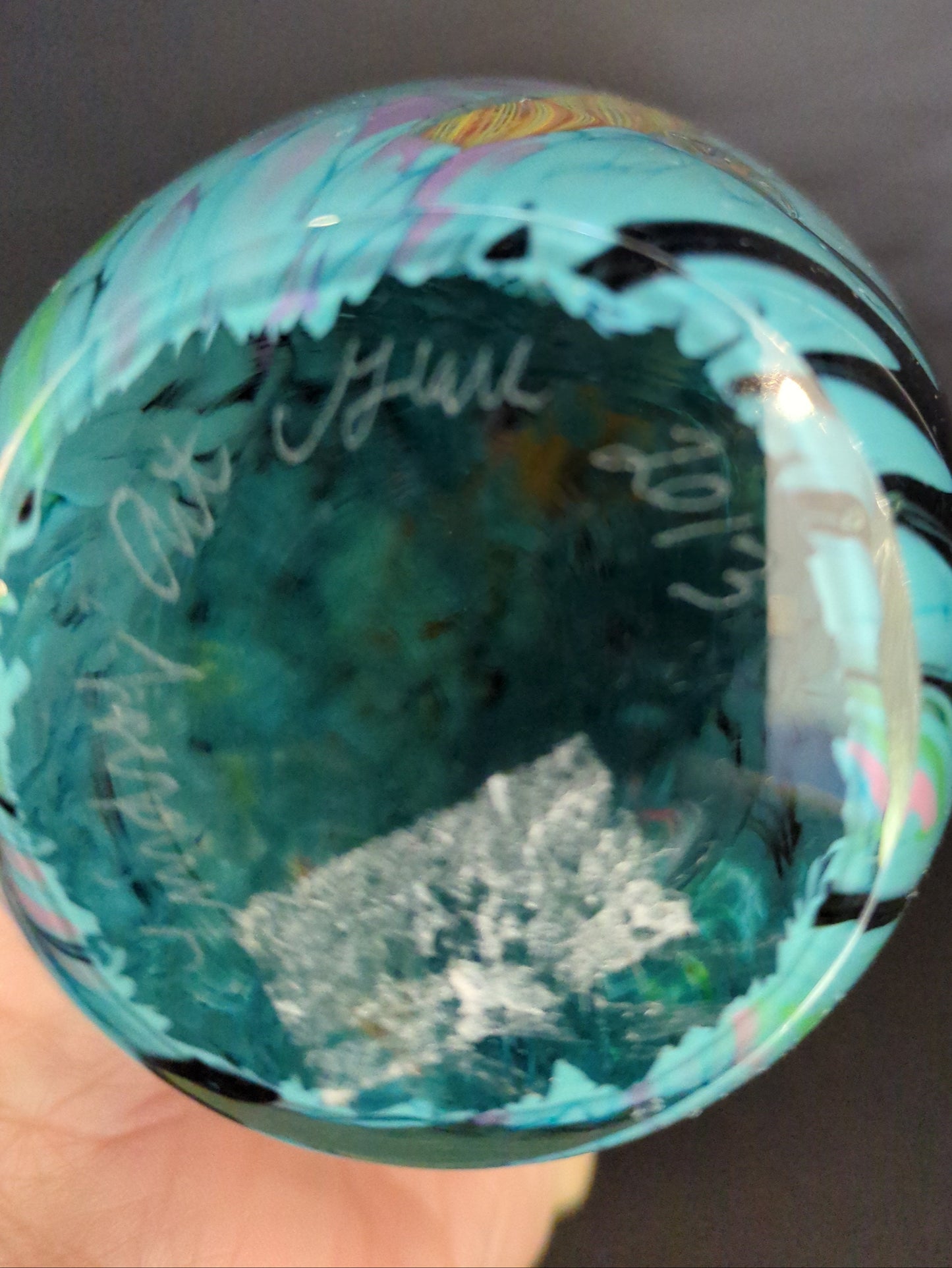 Turquoise glass paperweight held by a hand against a dark background