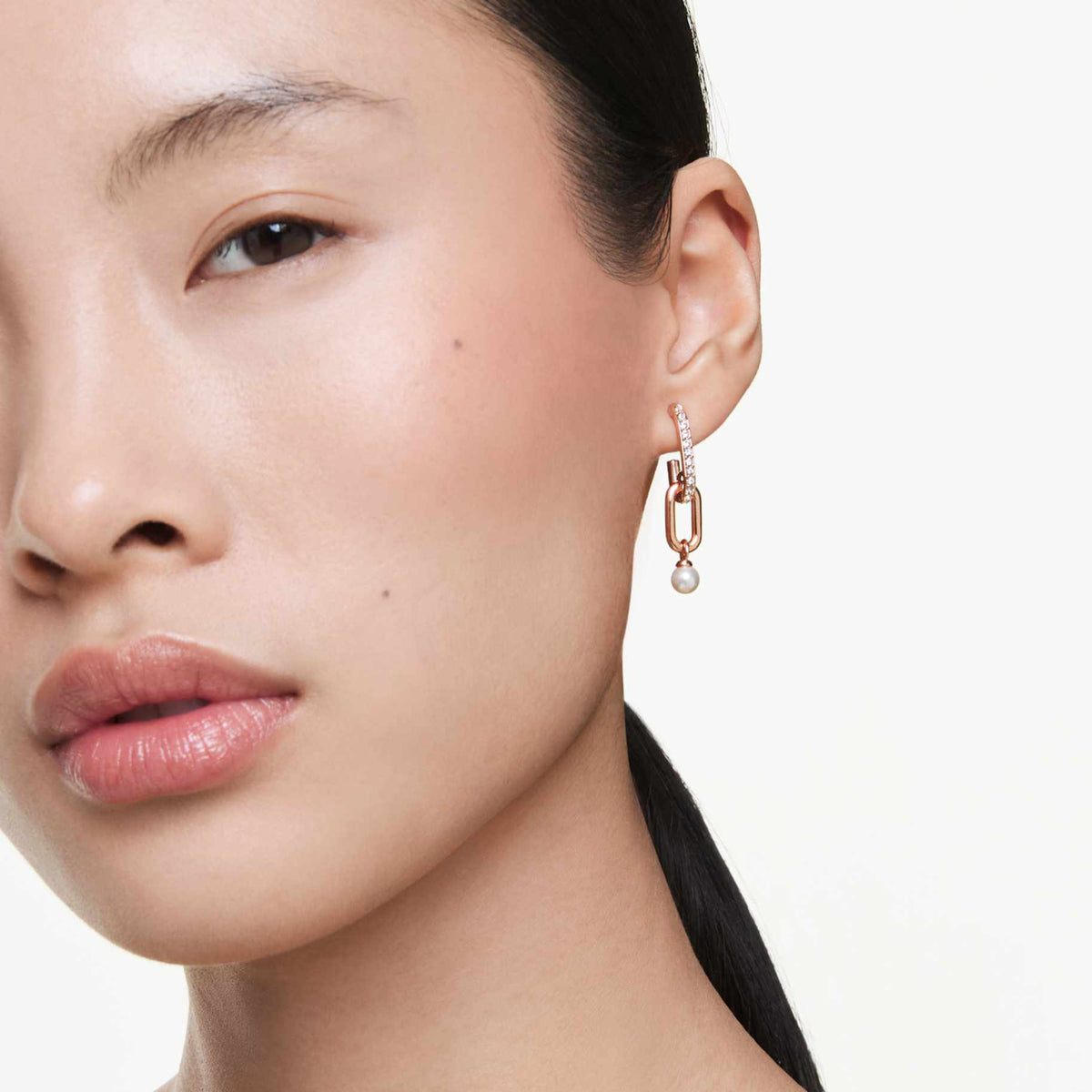 Model wearing a Swarovski Constella drop earring with rose gold-tone links, clear crystals, and a white pearl drop.