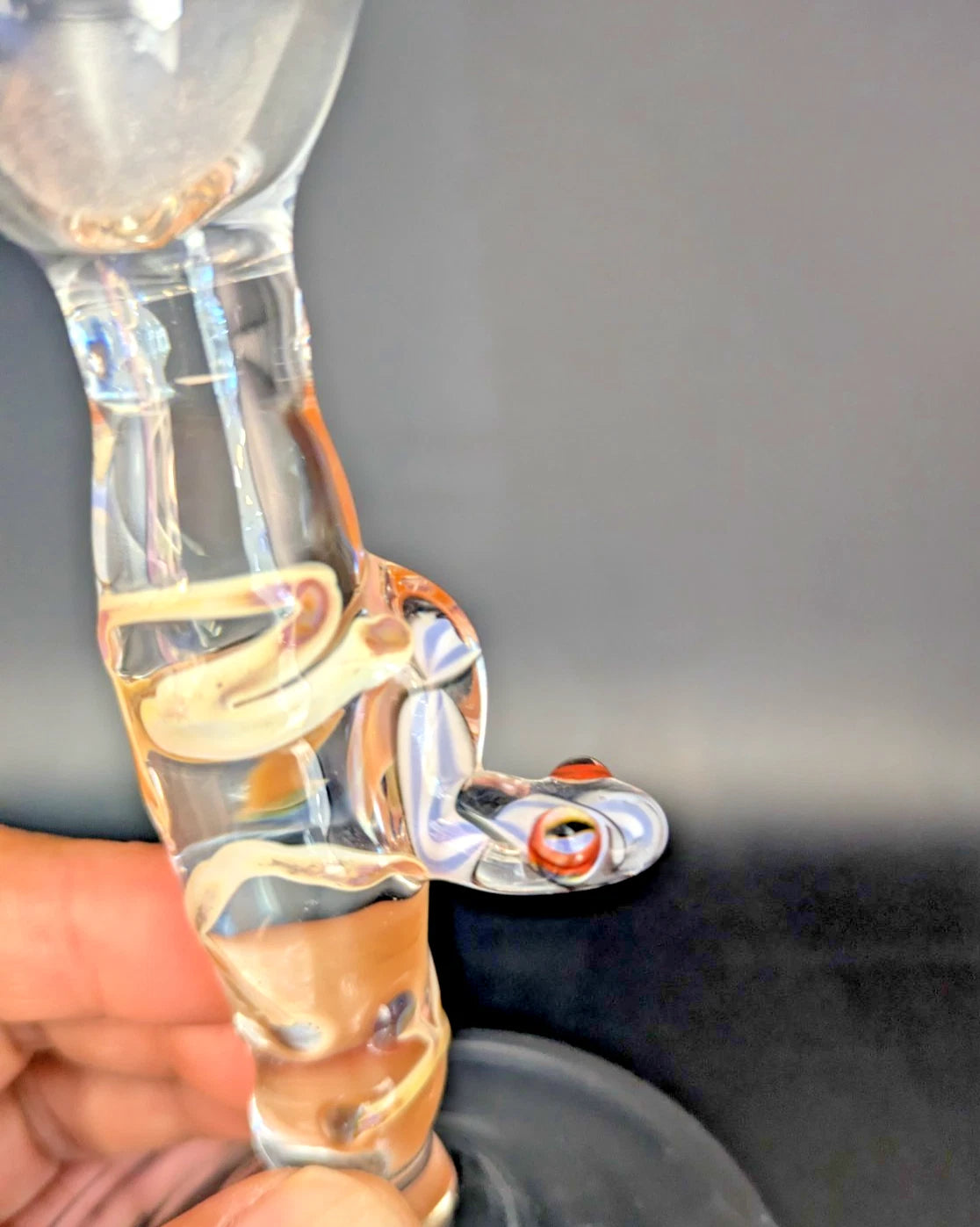 Glass pipe with a frog design held by a hand against a gray background
