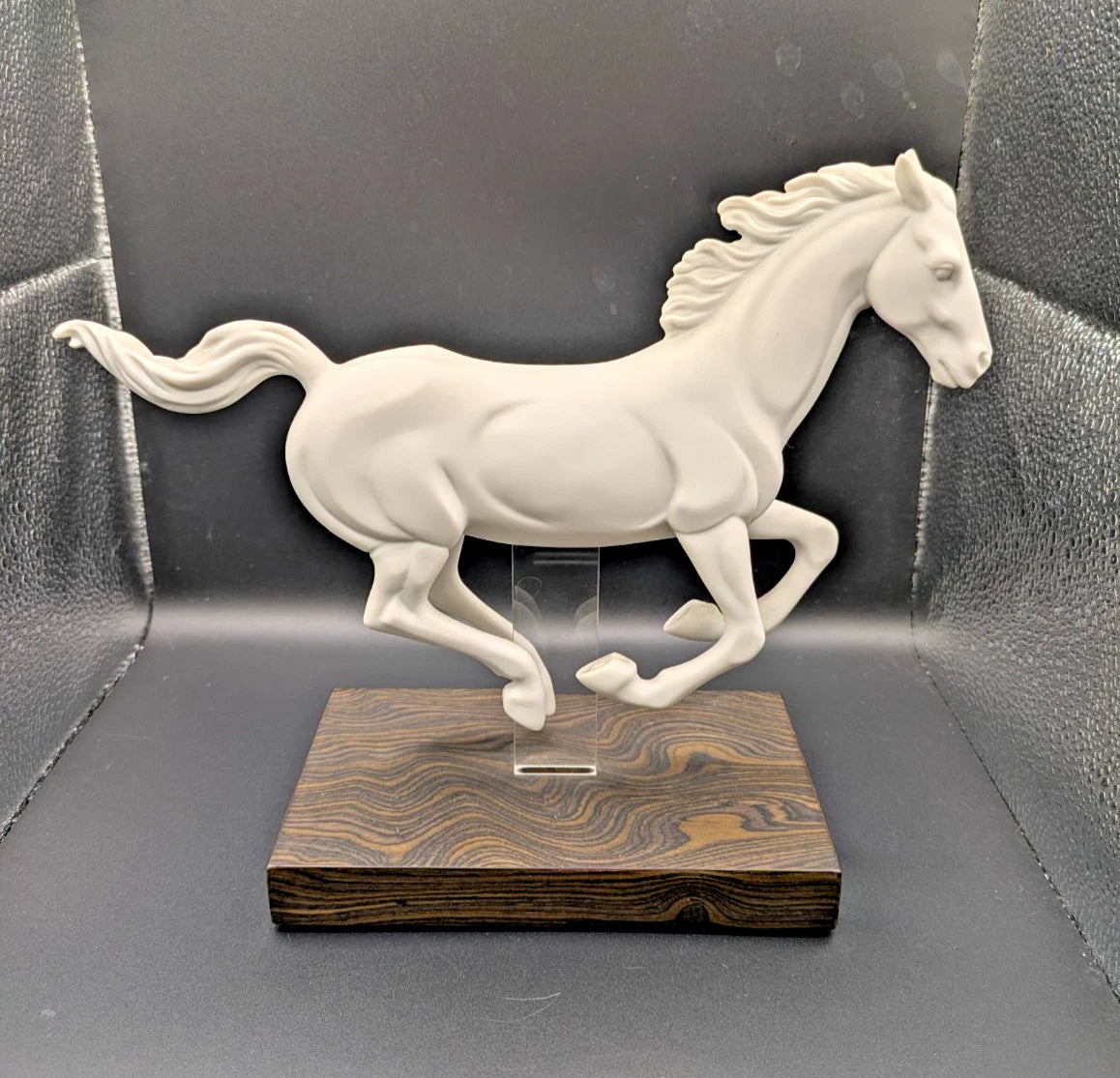 White horse sculpture on a wooden base against a gray background