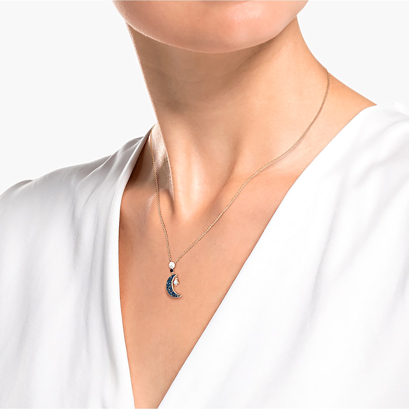 A rose gold-tone plated Swarovski pendant featuring a moon and star motif with blue crystals set in pavé on model.