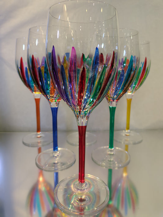 A set of multicolored wine glasses with a clear upper part and colorful lower part, with a reflective surface below.