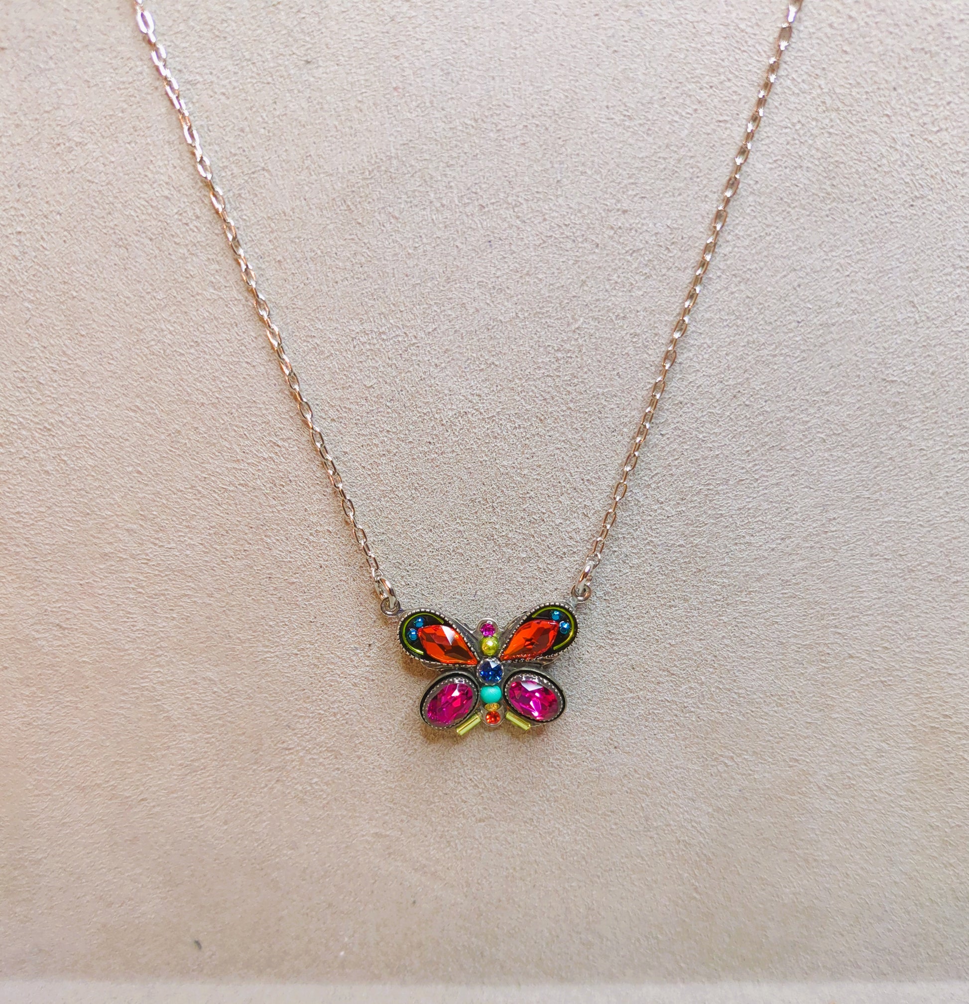 A colorful butterfly-shaped necklace with multicolored crystals and an antiqued steel chain on gray background.
