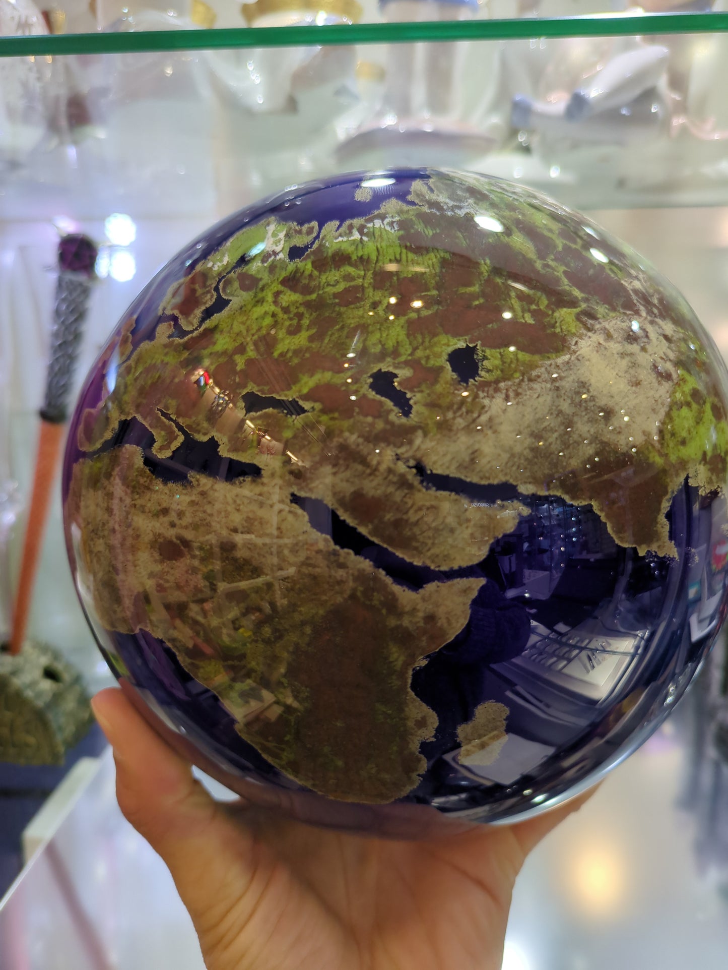 Hand holding a glass paperweight with a world map, blurred background