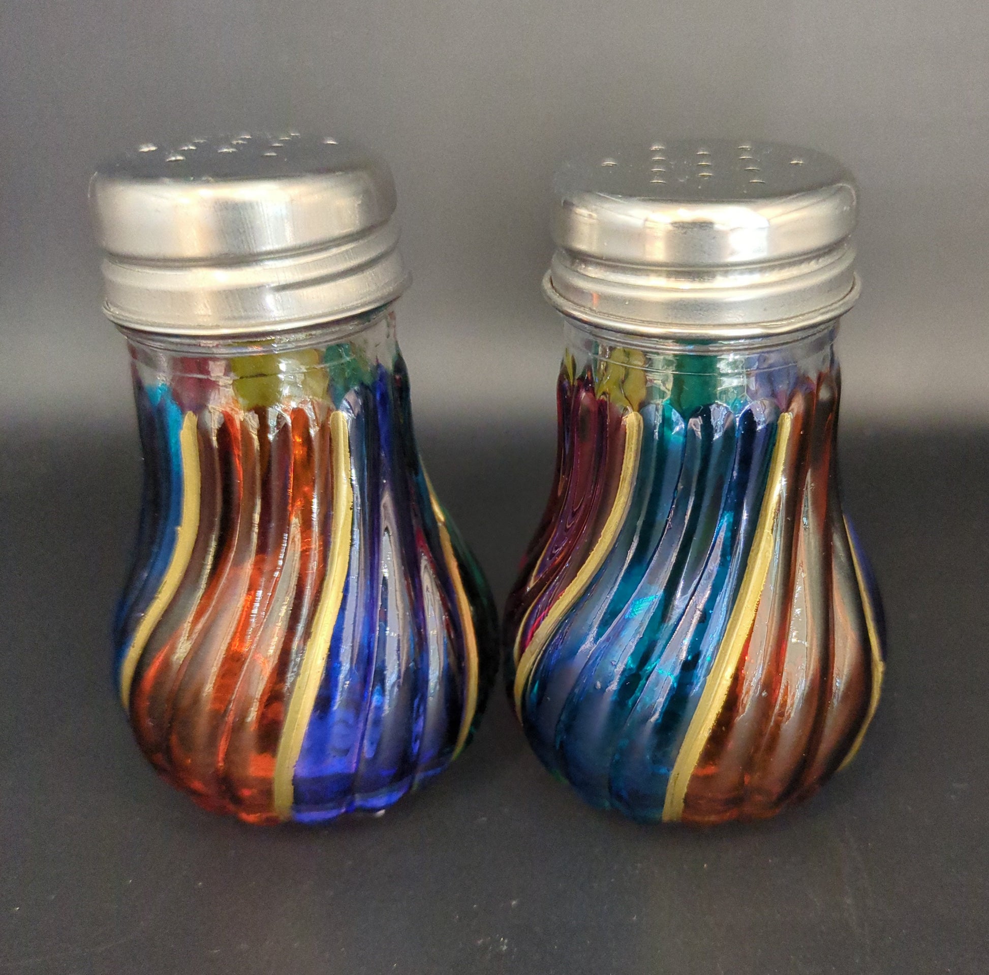 Colorful glass salt and pepper shakers on a dark surface