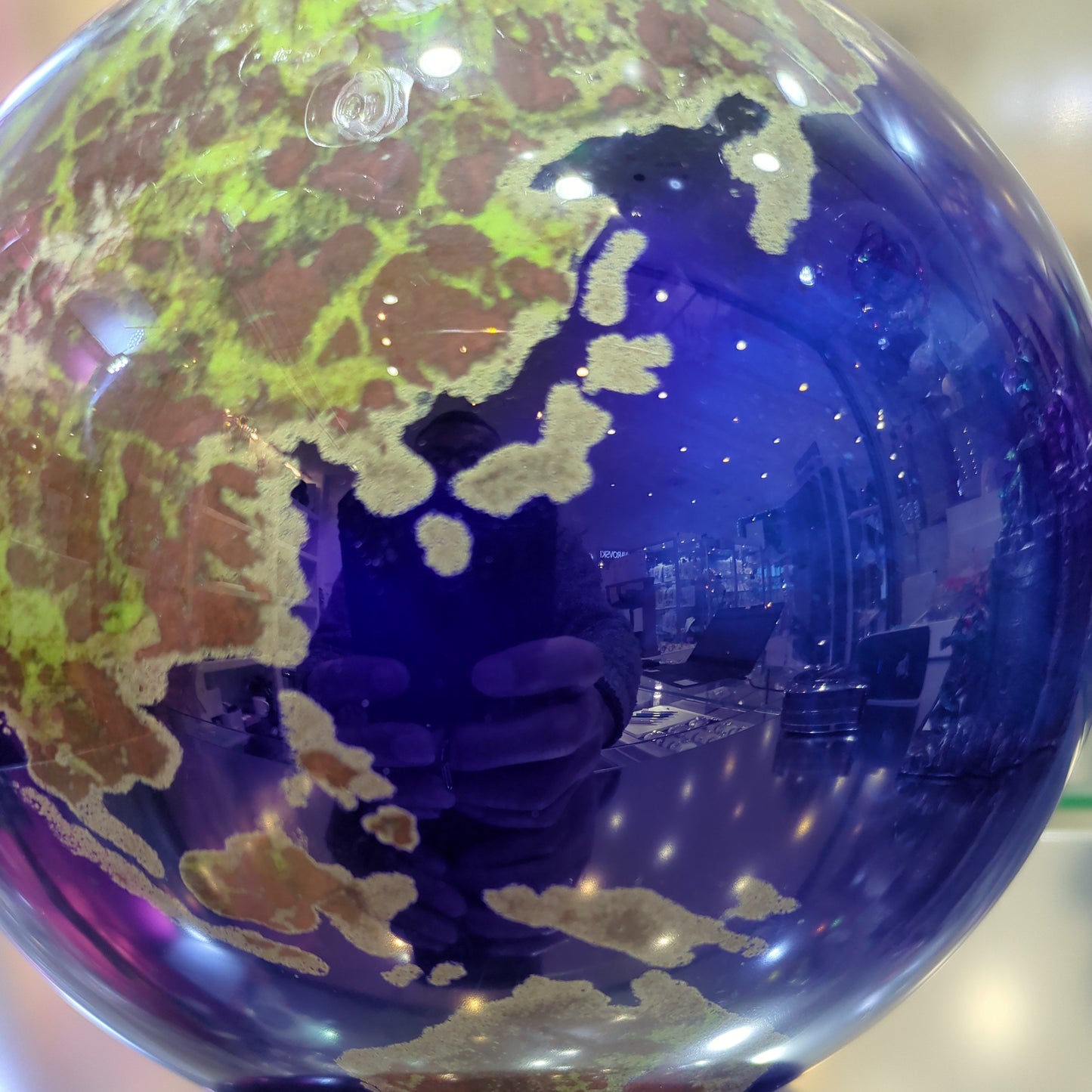 Close-up of a blue glass orb with world map design on a reflective surface.
