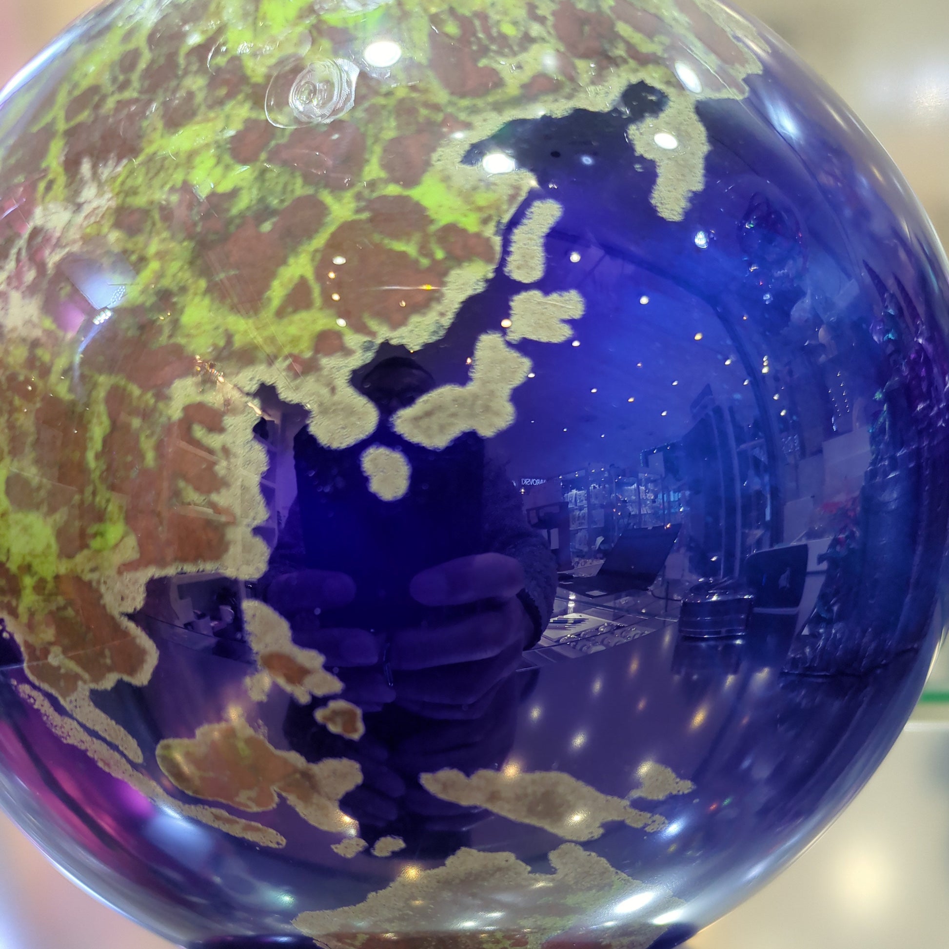 Close-up of a blue glass orb with world map design on a reflective surface.