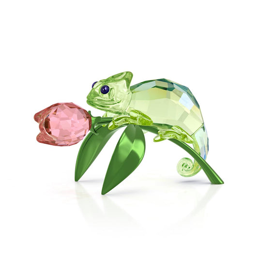 Crystal chameleon figurine on a pink flower with green leaves on a white background