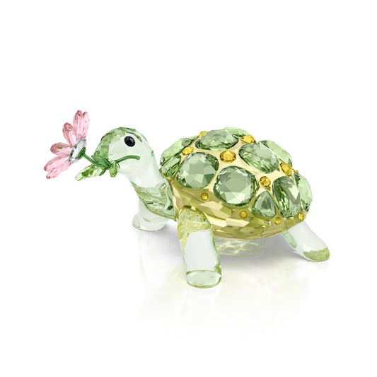 Crystal turtle figurine with green gemstones and a pink flower on a white background