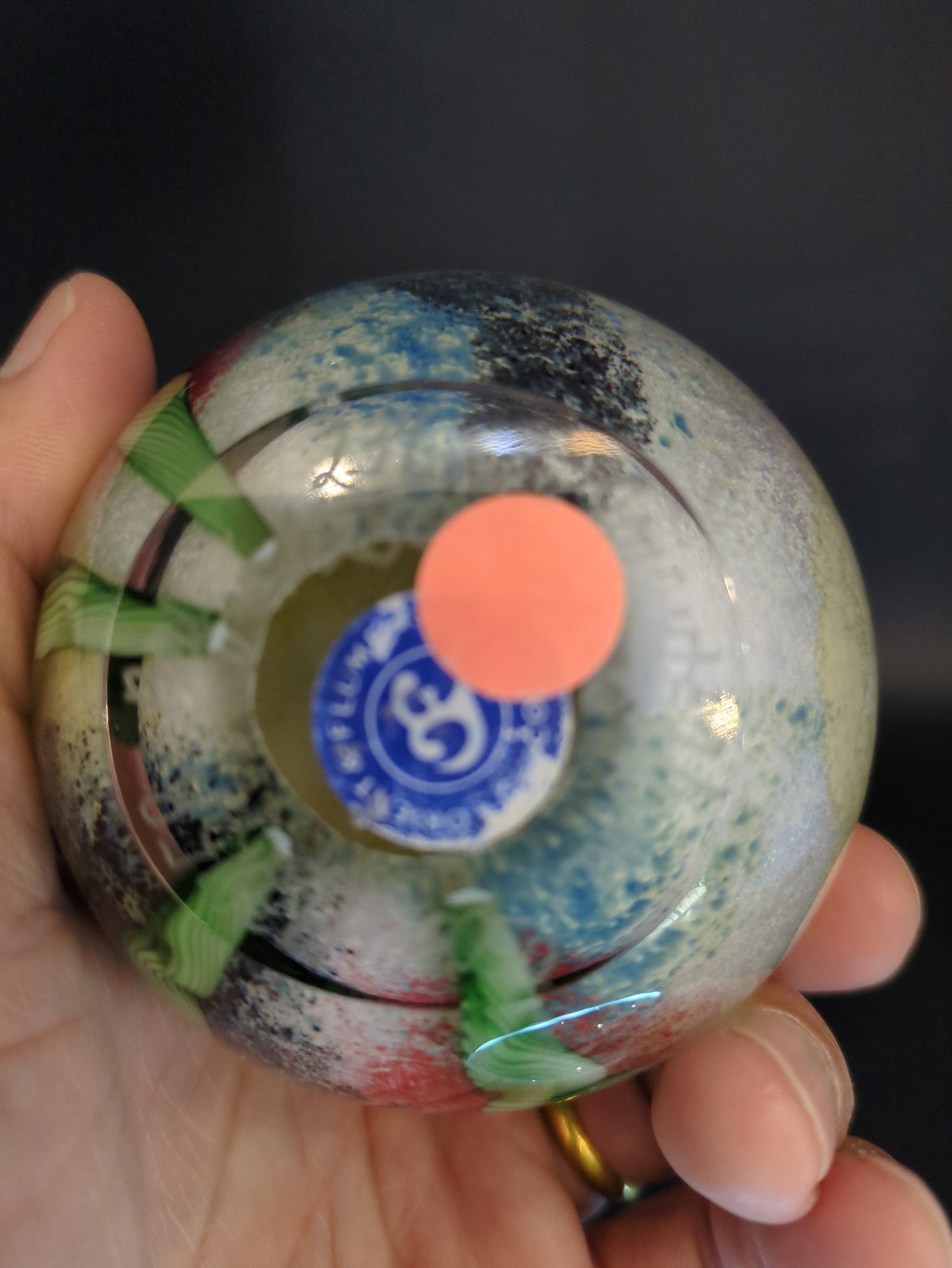 Colorful glass paperweight with a brand logo held in a hand against a dark background