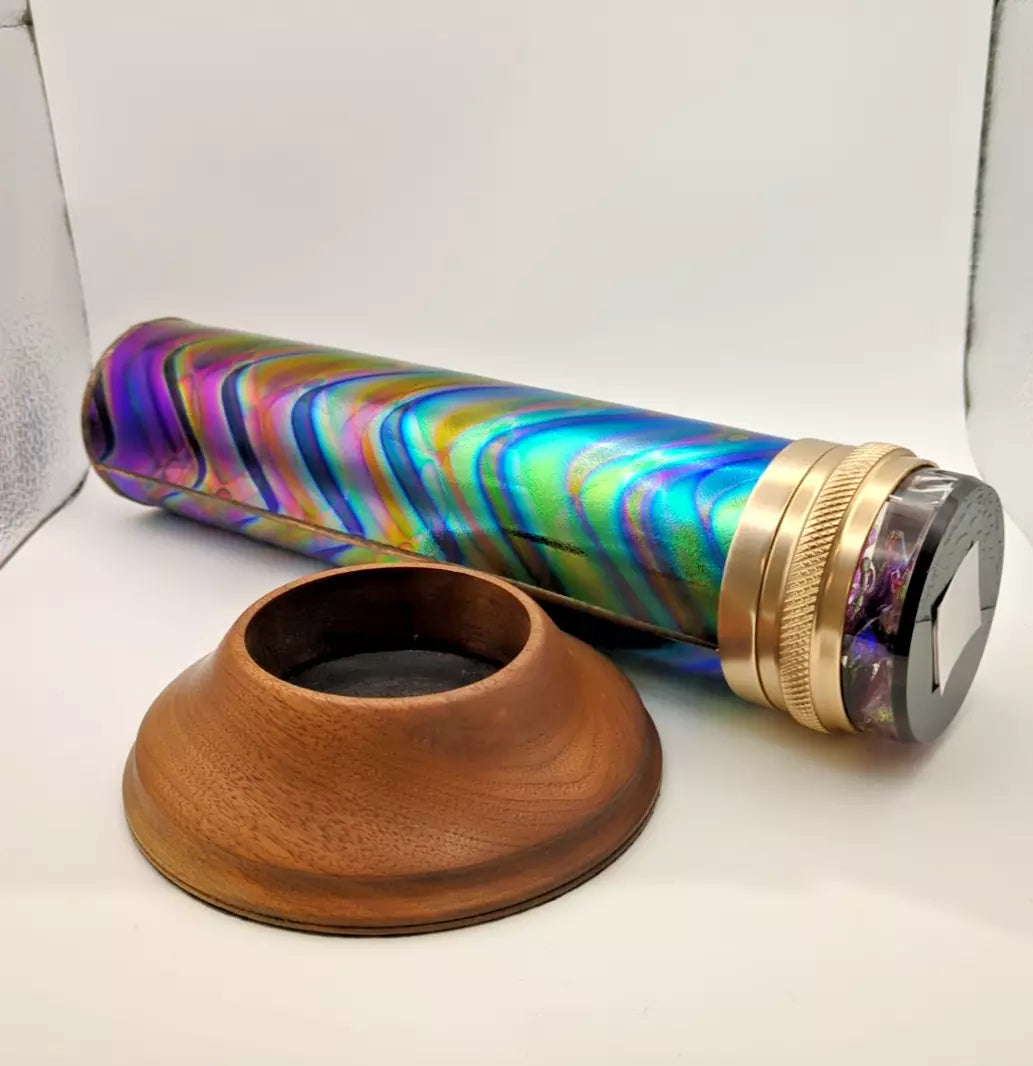 Colorful cylindrical object with gold accents and a wooden base on a white surface