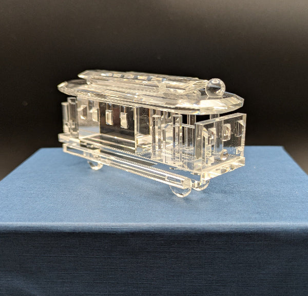 Clear glass model of a train on a blue box against a dark background