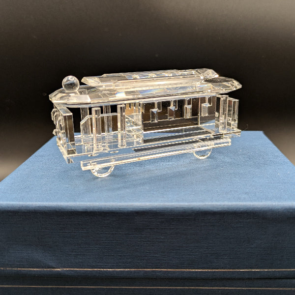 Clear glass model of a train car on a blue cushion with a dark background