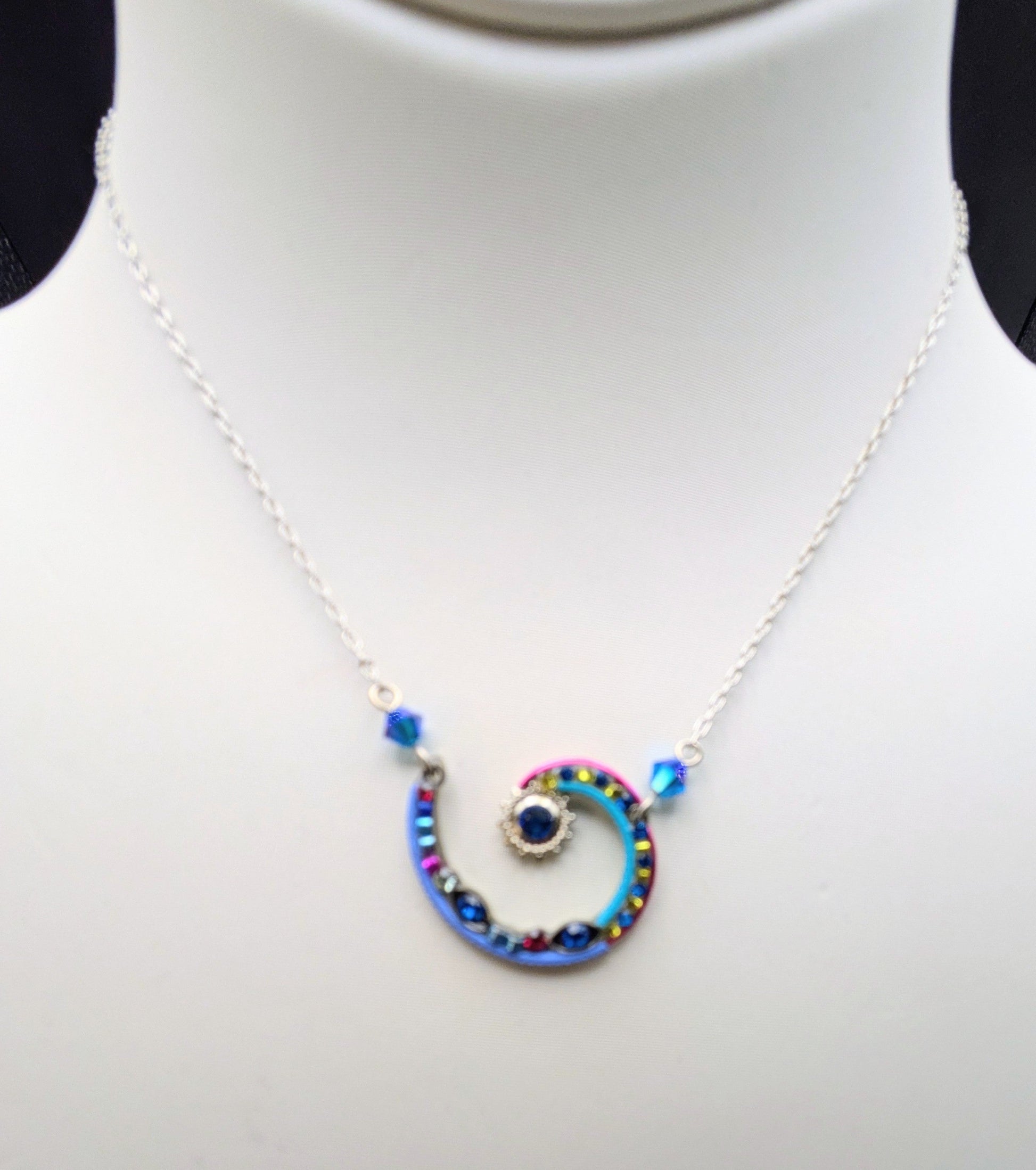 A silver chain necklace with a spiral pendant featuring blue, red, and yellow beads, displayed on a white mannequin bust.