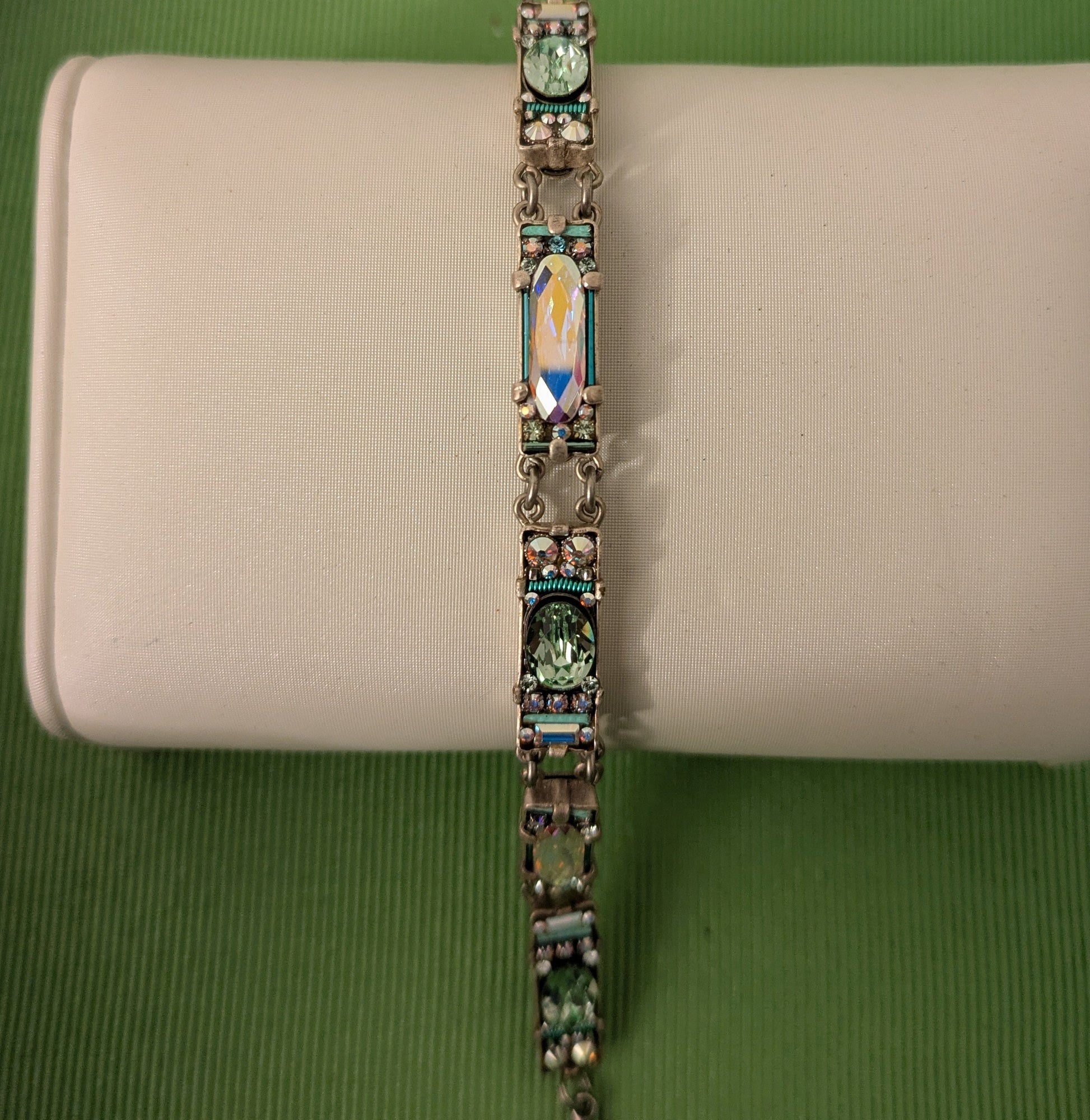 Bracelet with green gemstones on a beige cushion against a green background