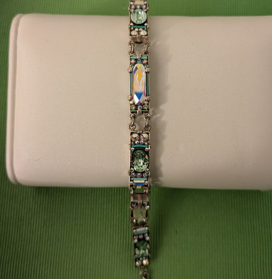 Bracelet with green gemstones on a beige cushion against a green background
