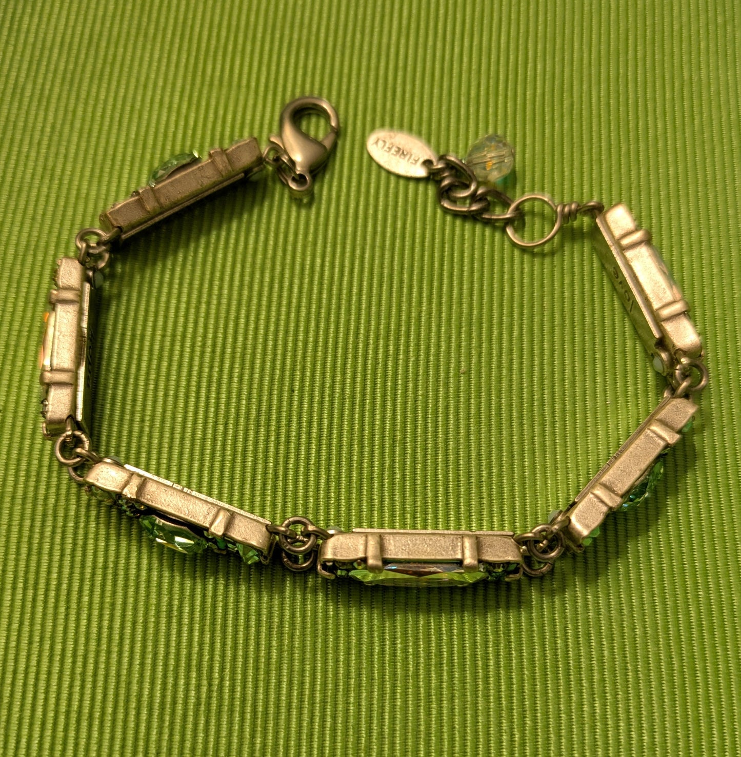 Silver bracelet with green stones on a green textured surface