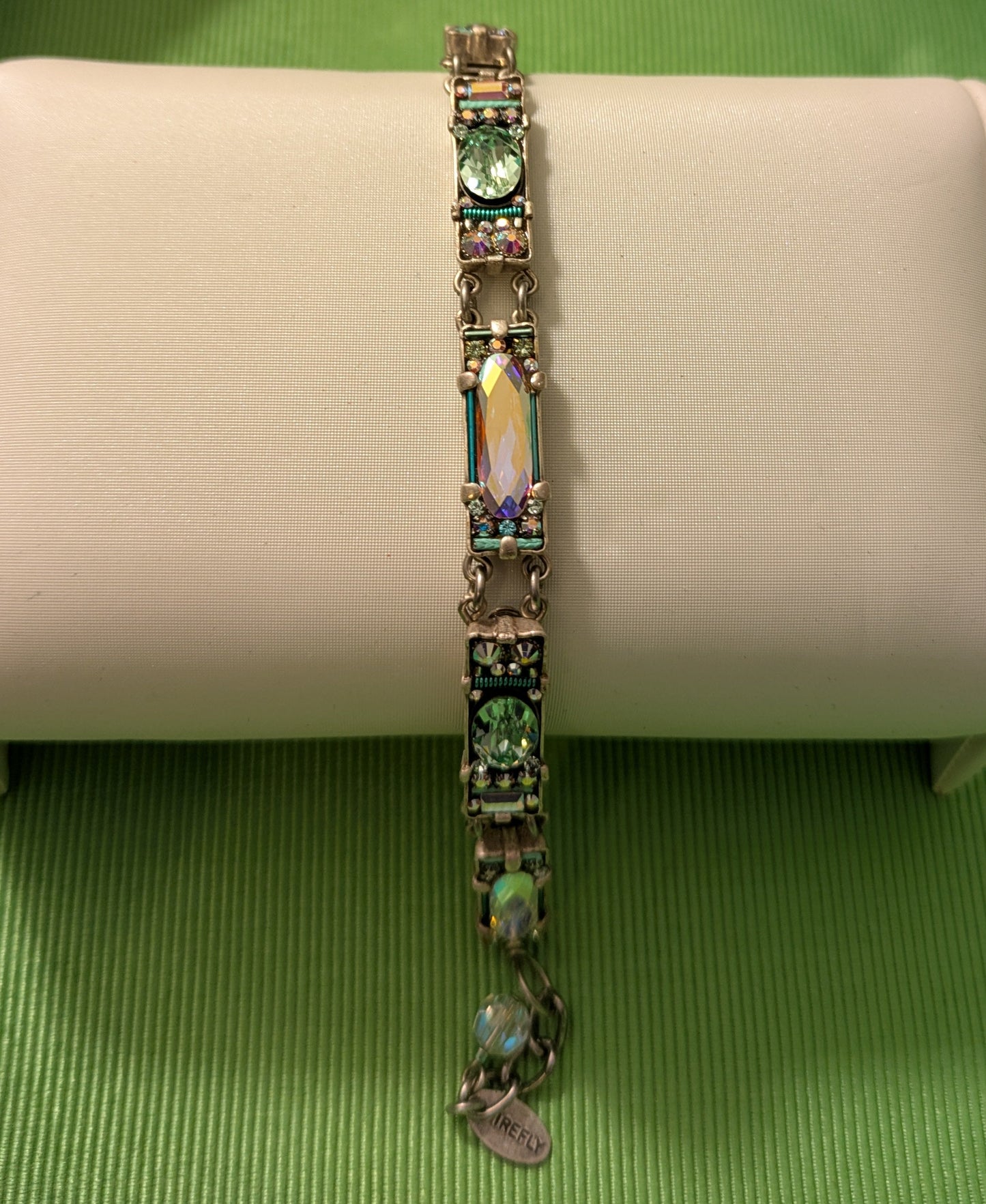 Bracelet with green gemstones on a beige cushion against a green box background