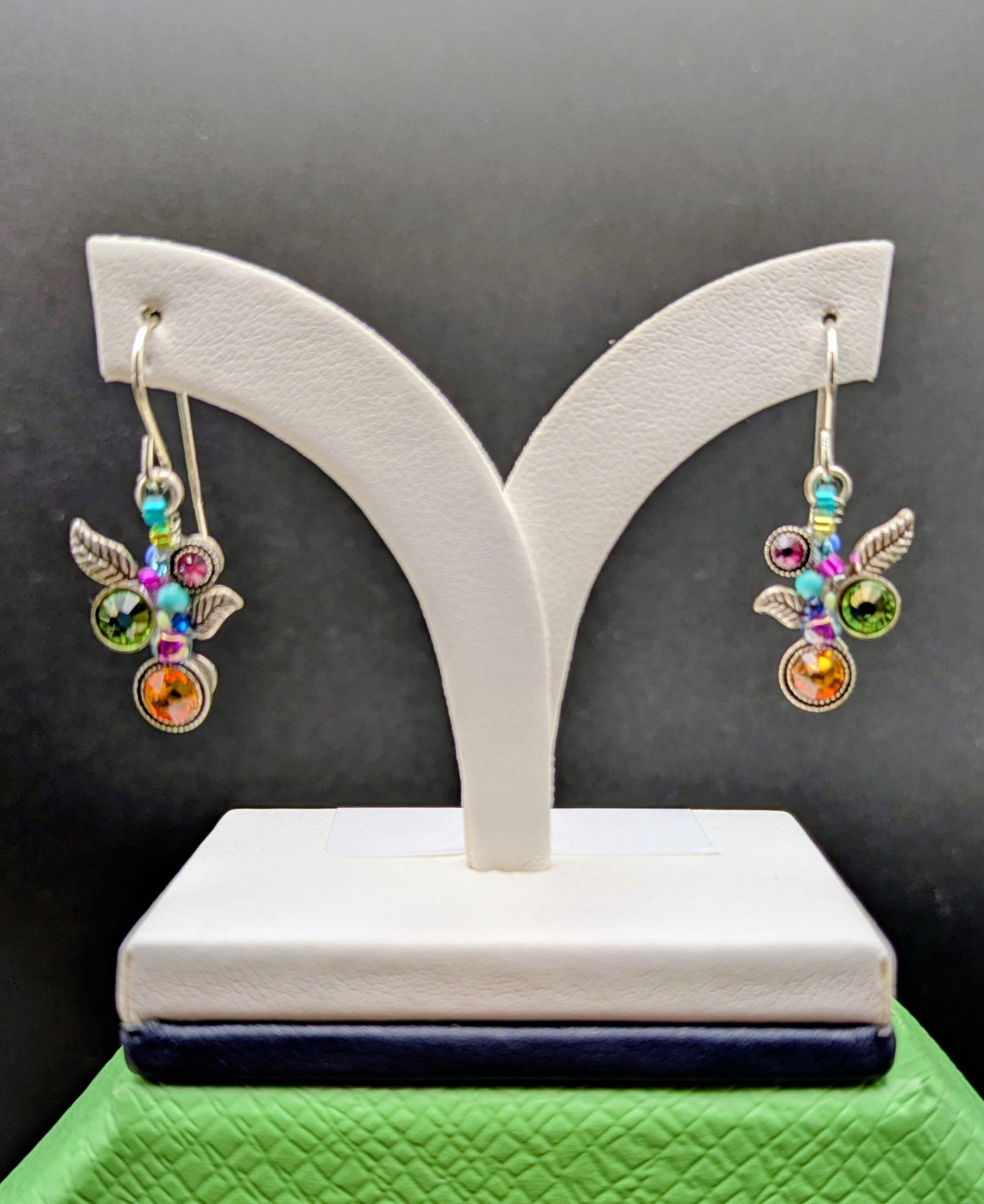 Multicolored gemstone earrings on a white stand against a dark background