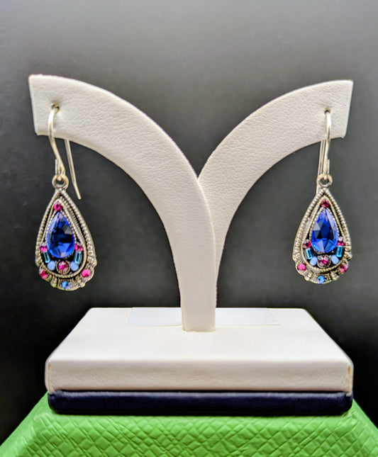 Teardrop-shaped earrings with gemstones on a white stand against a dark background
