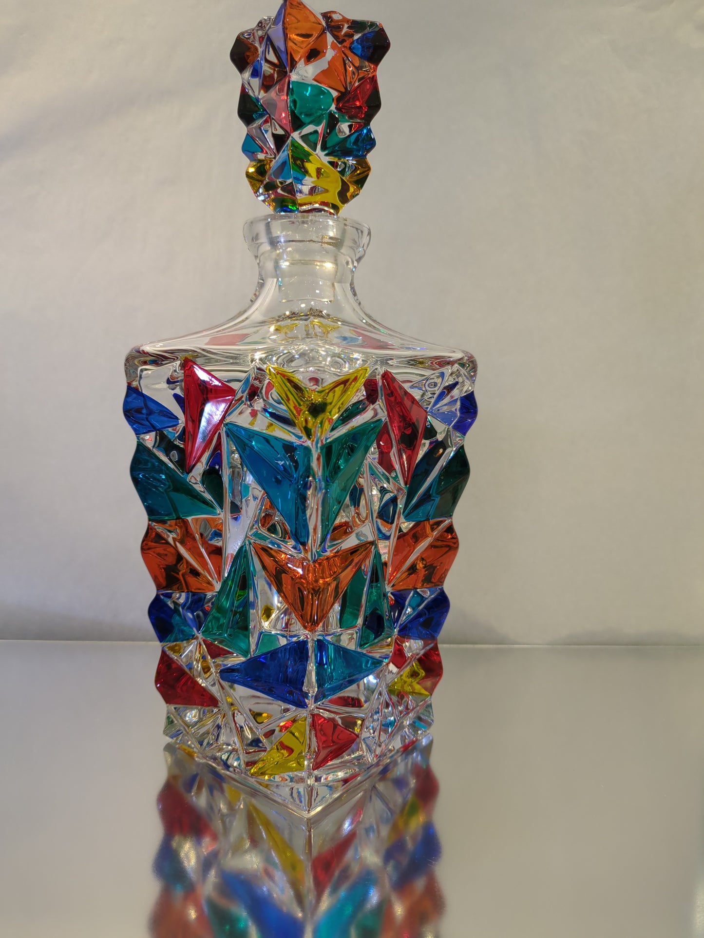 A tall, multicolored Murano glass decanter with a geometric pattern, displaying a range of colors including blue, red, and green.