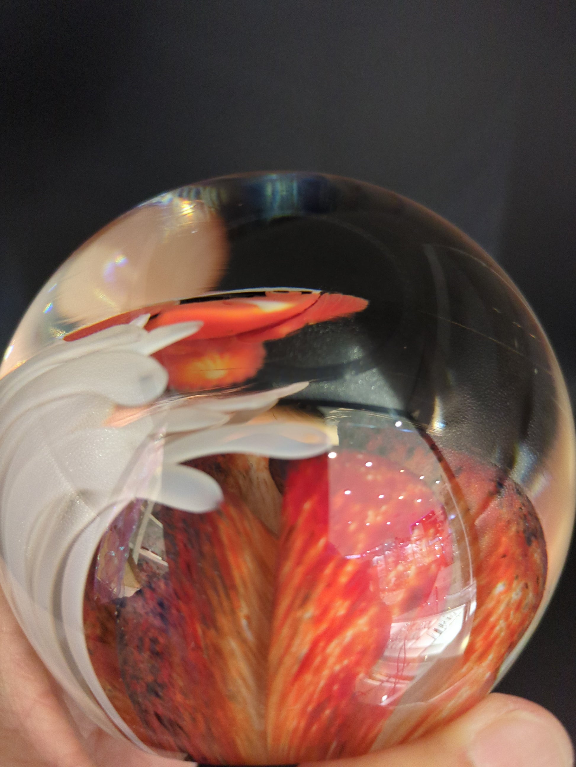 Glass sphere with a red and orange abstract design held by a hand against a dark background