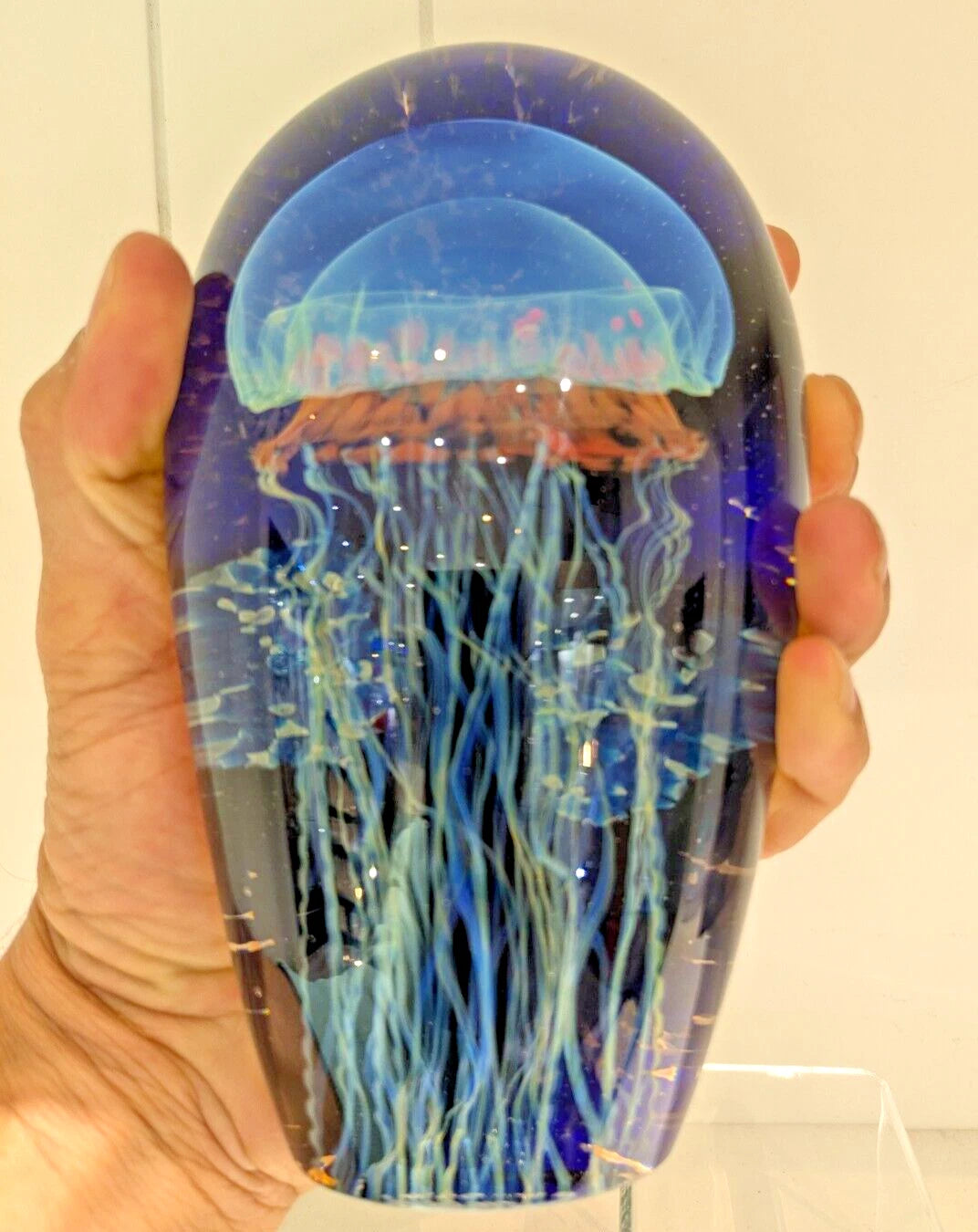 Hand holding a transparent satava jellyfish figure with blue and orange colors.