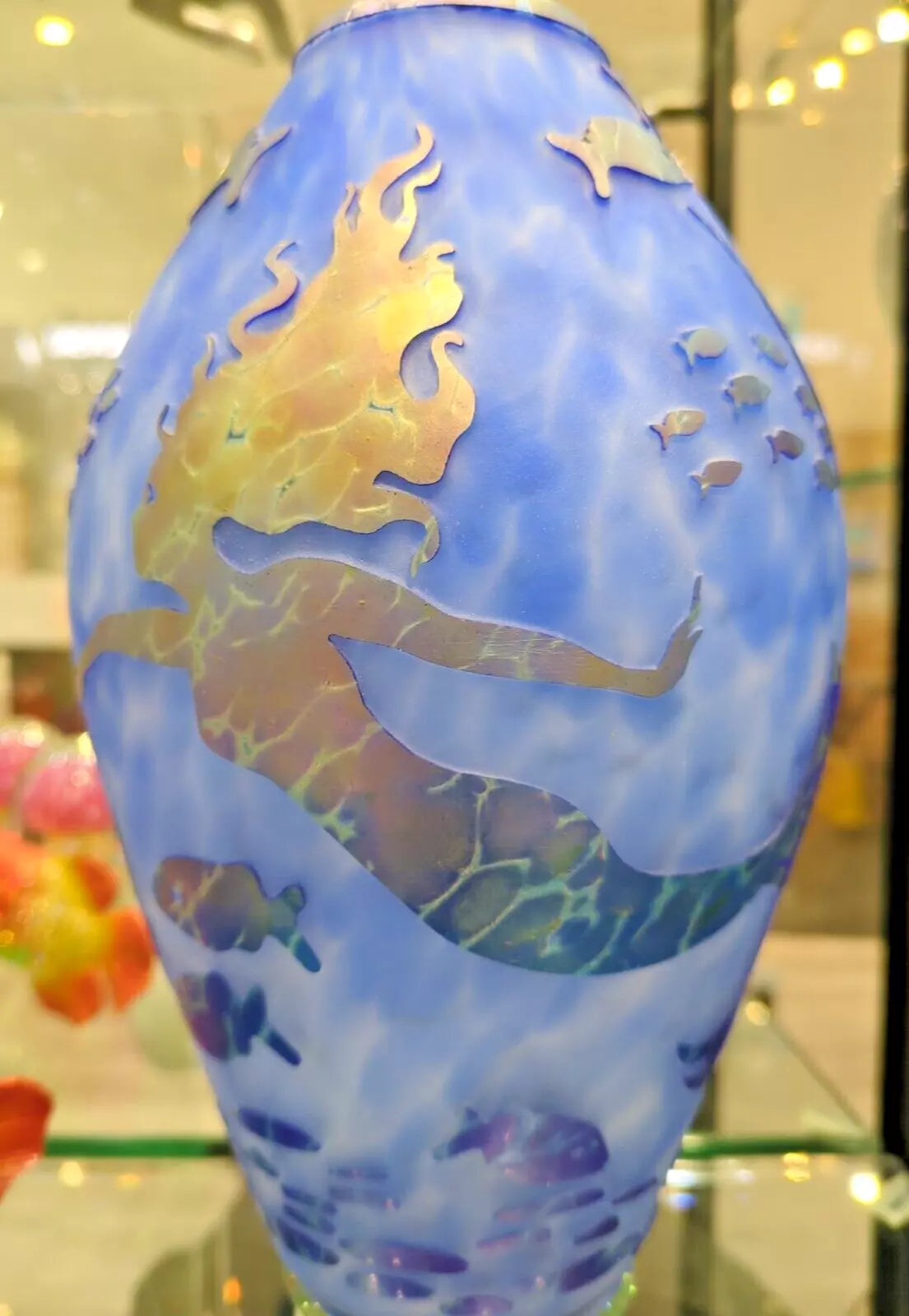 A blue art glass vase with etched gold design of a mermaid sitting on a leaf.