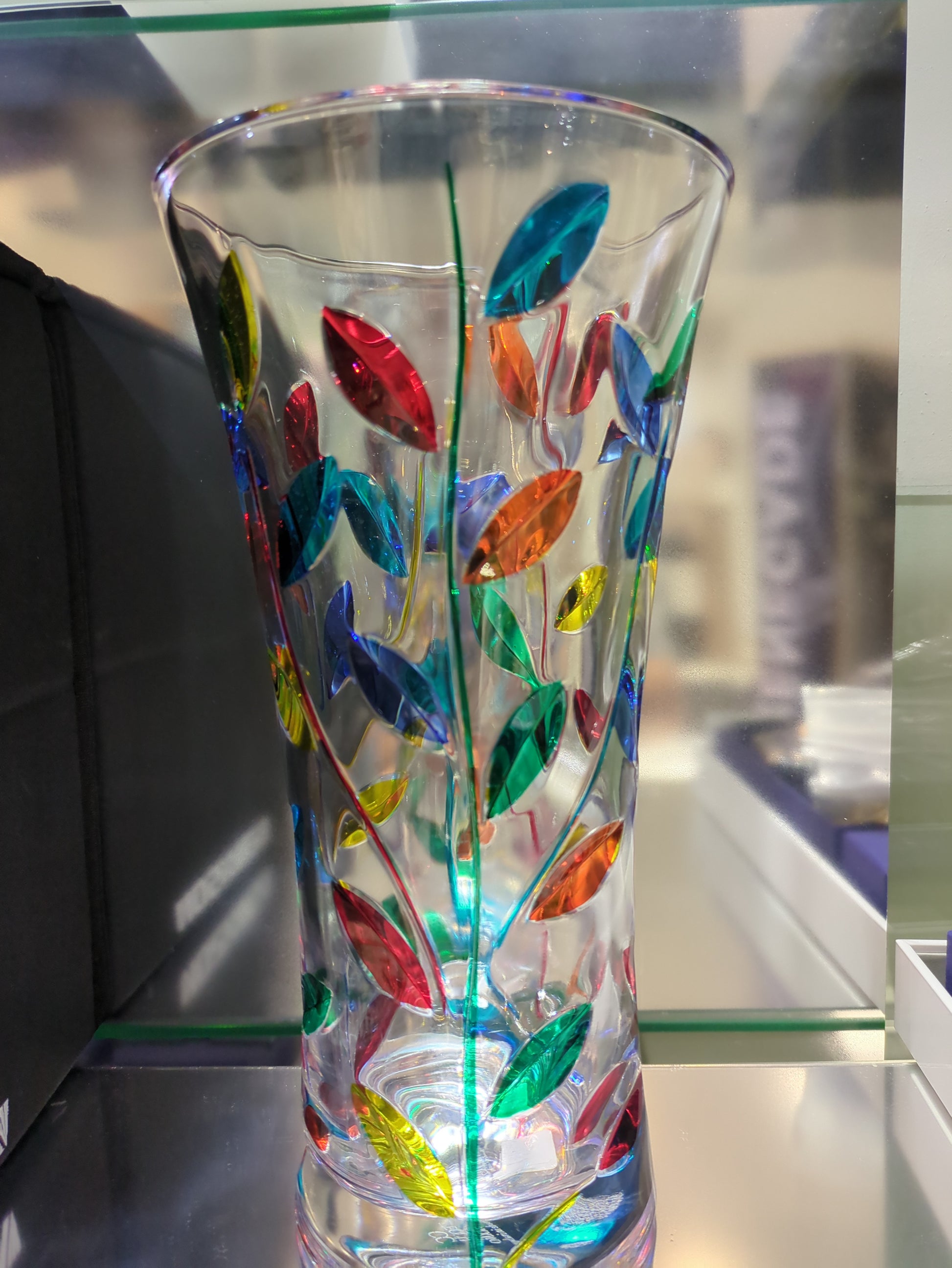 Glass vase with colorful leaf patterns on a reflective surface