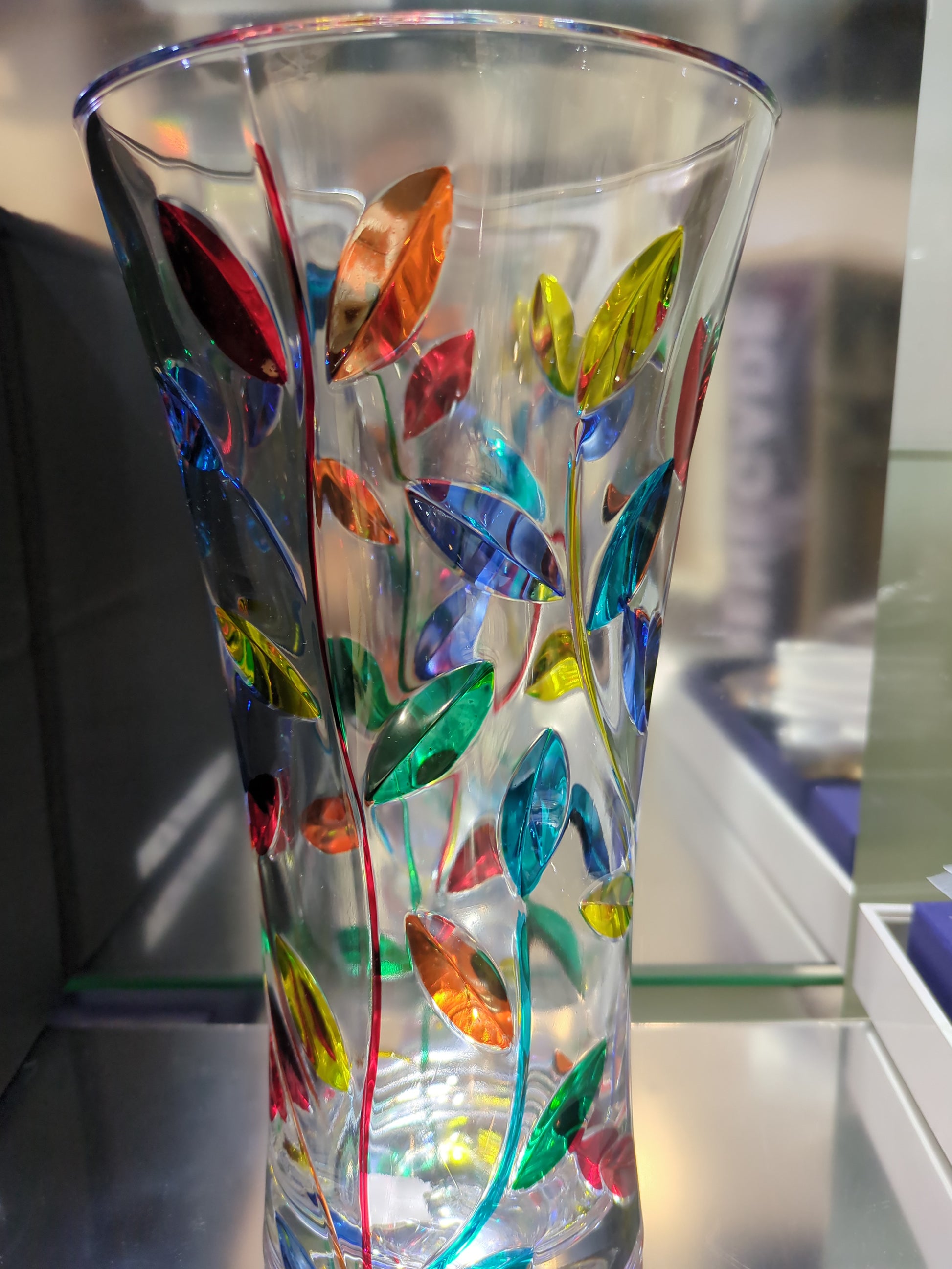 Decorative glass vase with colorful leaf patterns on a blurred background