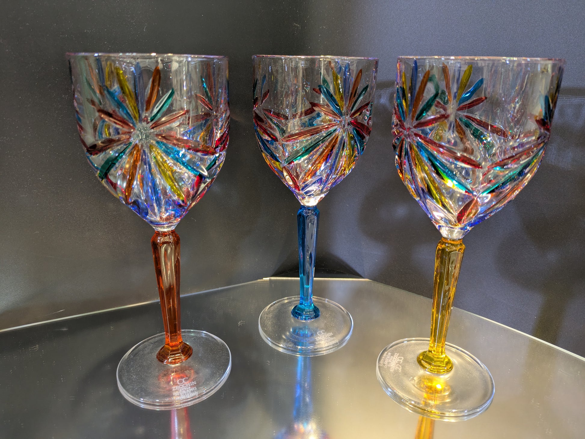 A set of three multicolored wine glasses with a geometric pattern on a reflective surface.