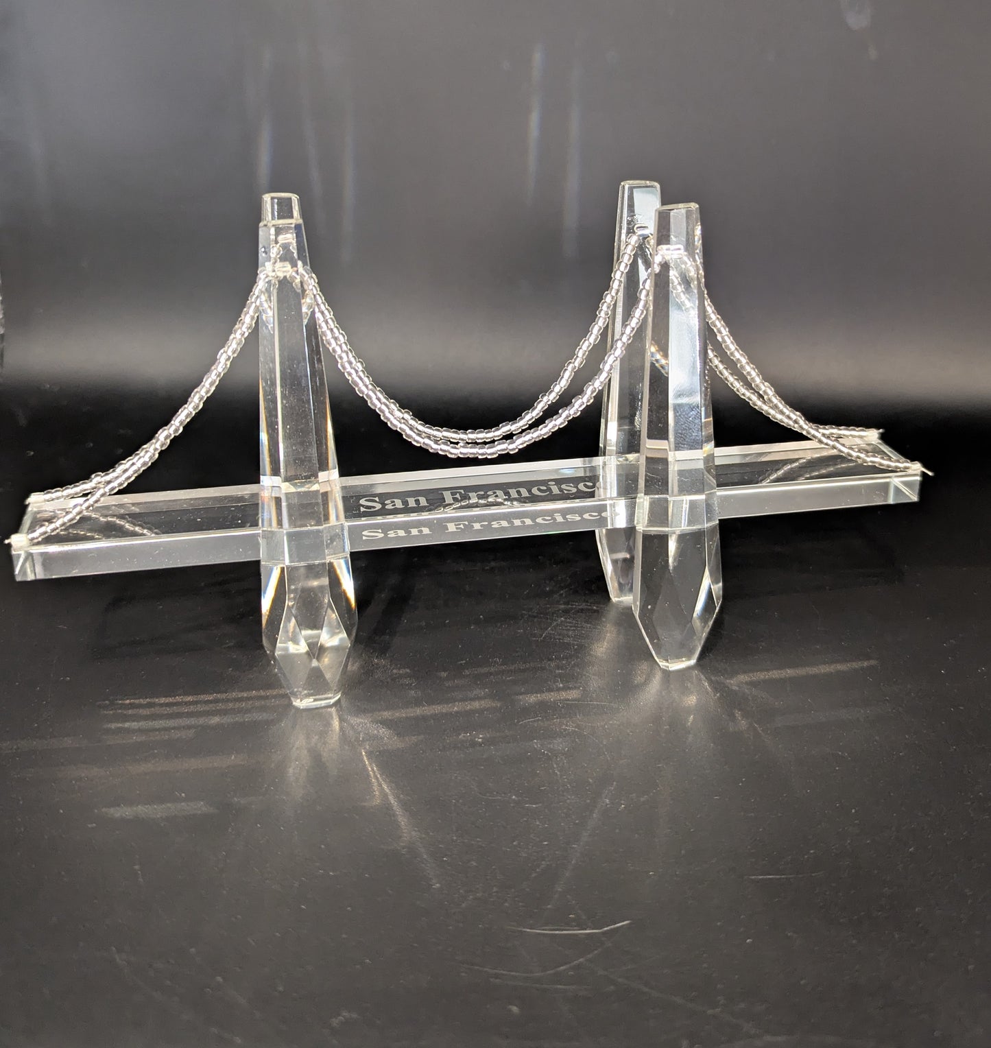 Model of a suspension bridge with 'San Leandro' and 'San Francisco' text on a black background