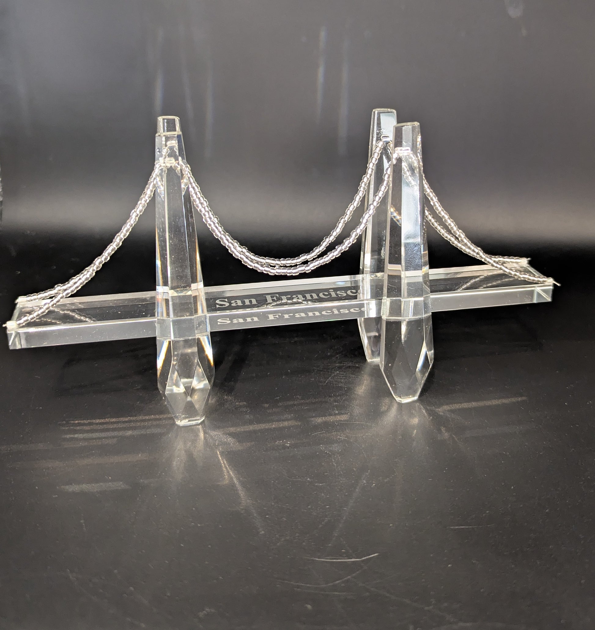 Model of a suspension bridge with 'San Leandro' and 'San Francisco' text on a black background