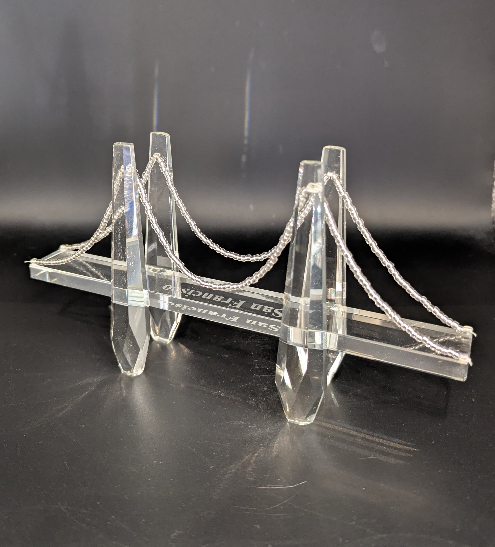 Model of a suspension bridge made of clear acrylic on a dark background