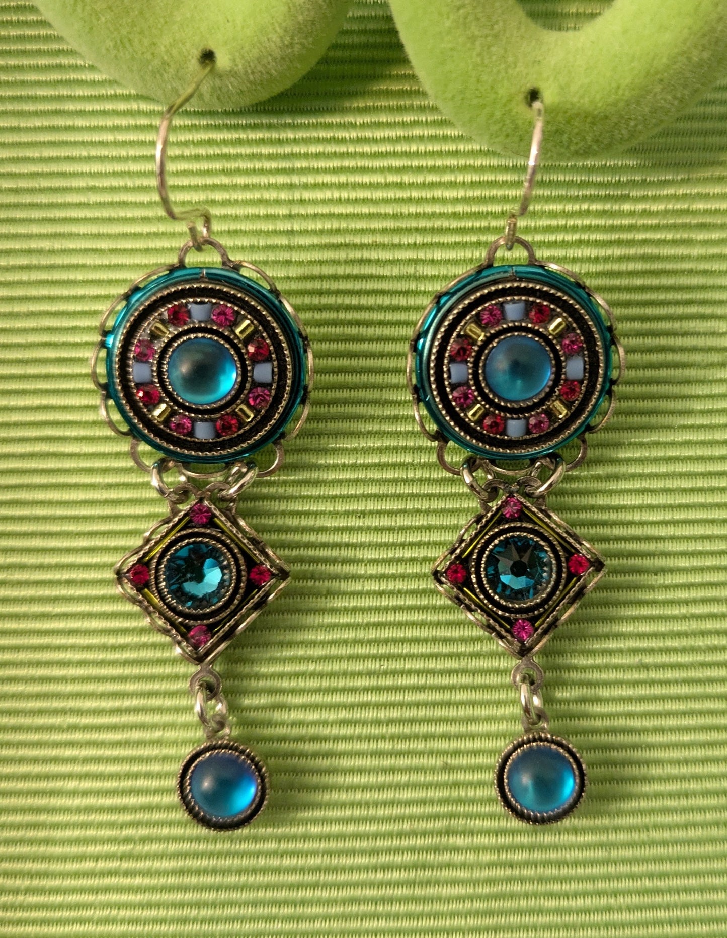 Pair of earrings with colorful gemstones on a green textured surface