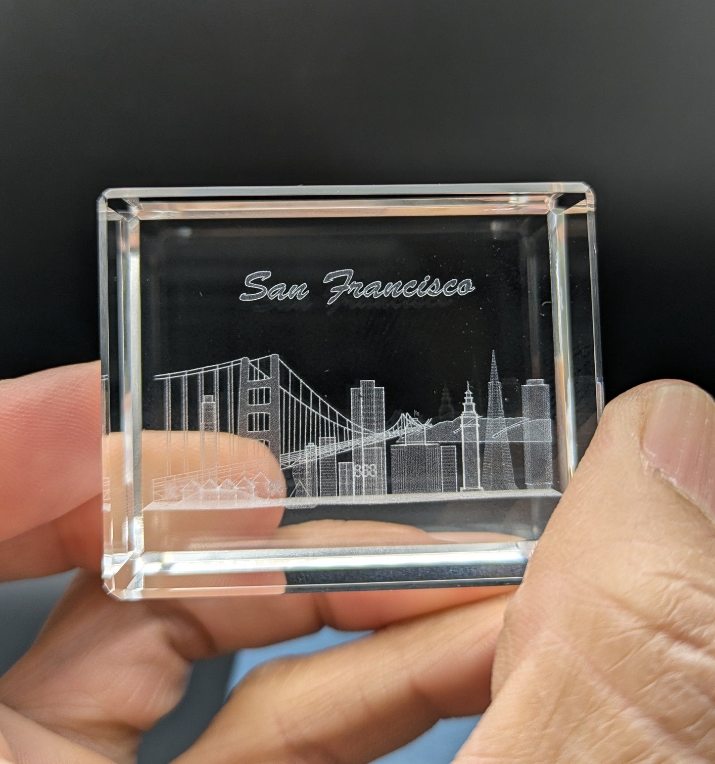 Clear crystal with engraved San Francisco skyline held in a hand against a dark background