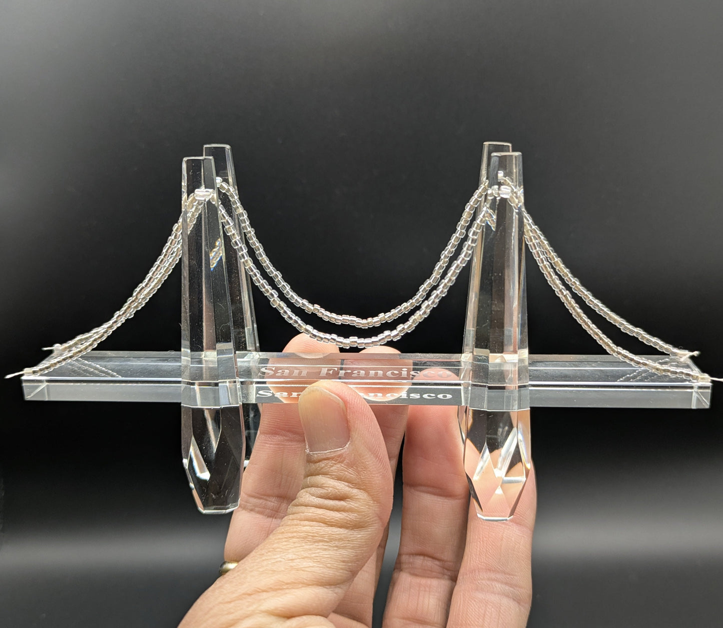 Model of a suspension bridge held in a hand against a black background