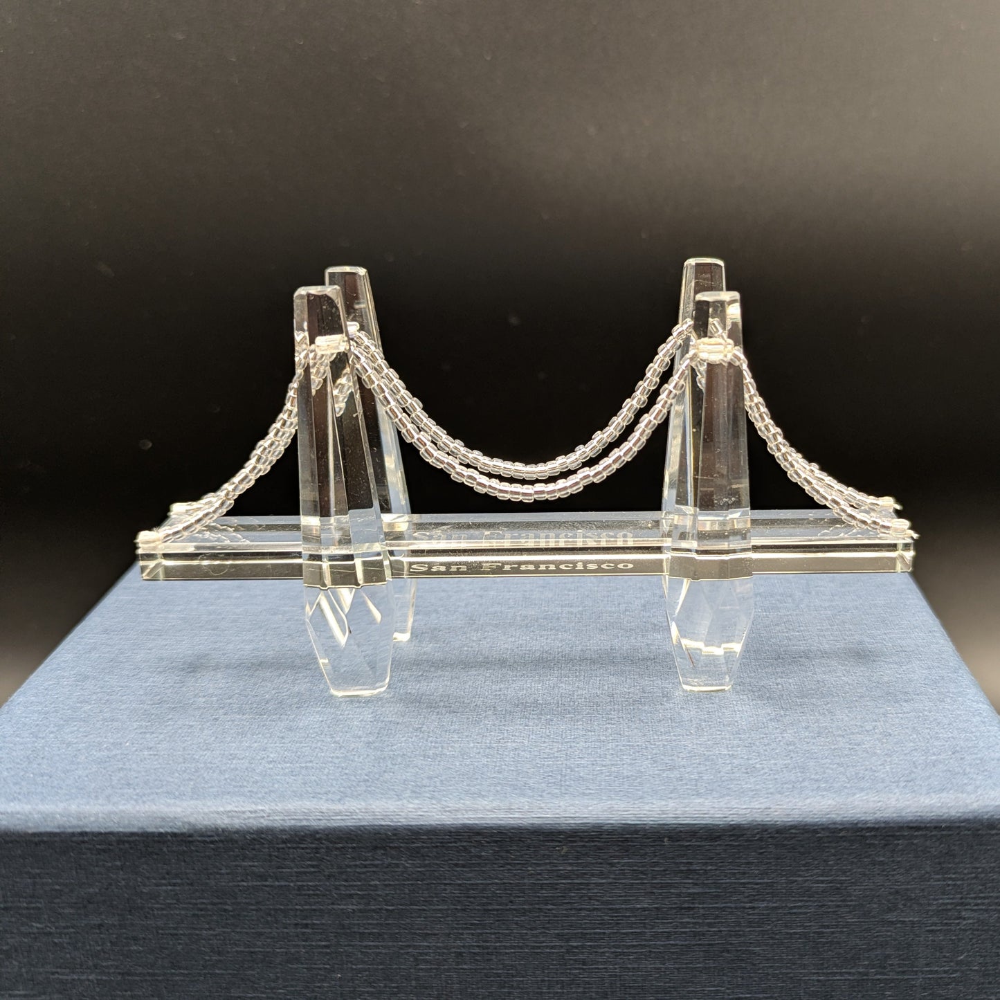 Model of a suspension bridge on a blue stand with a dark background