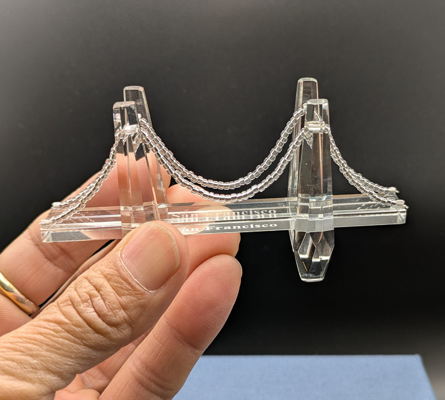 Clear 3D-printed bridge model held by a hand against a dark background