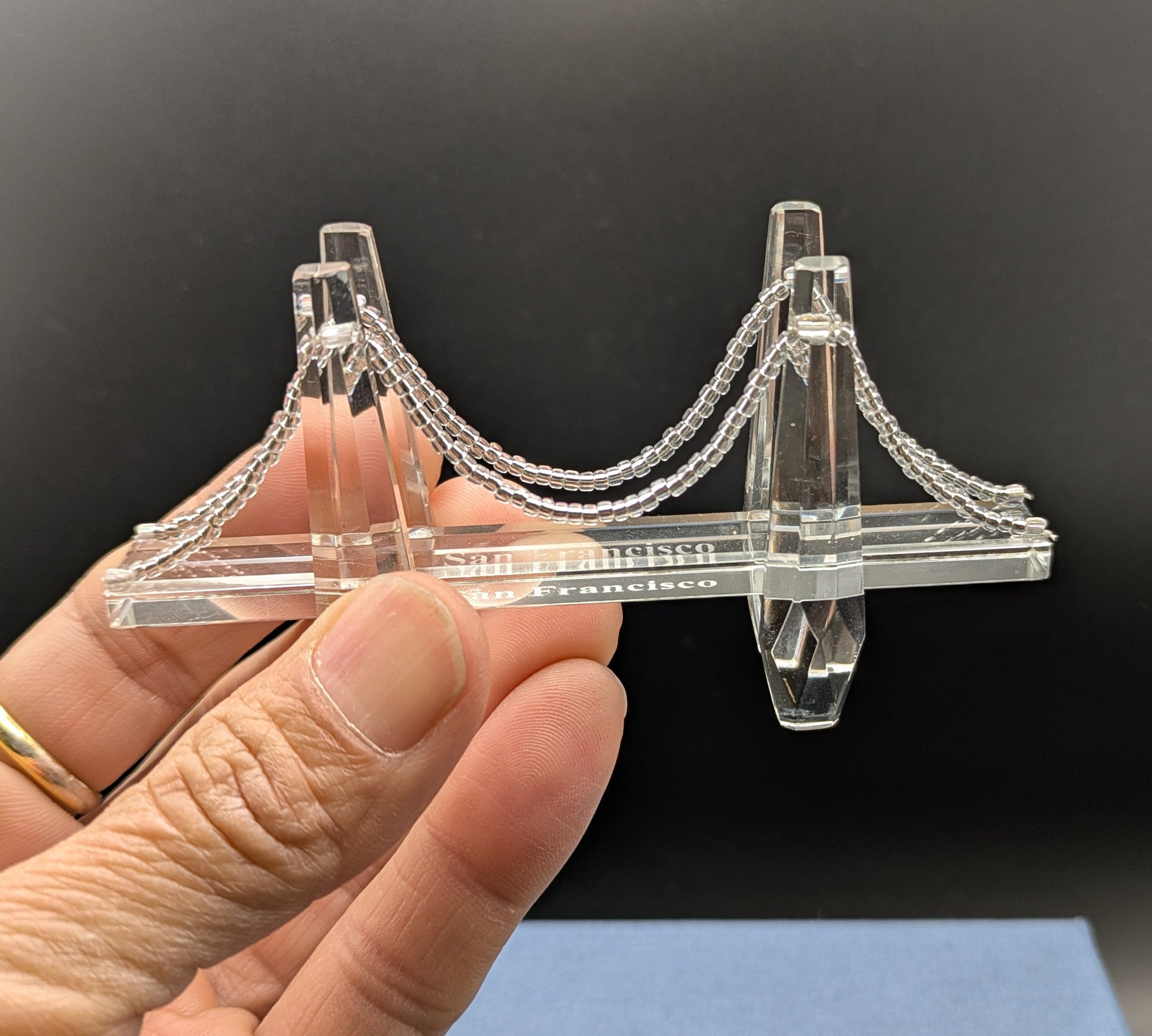 Clear 3D-printed bridge model held by a hand against a dark background
