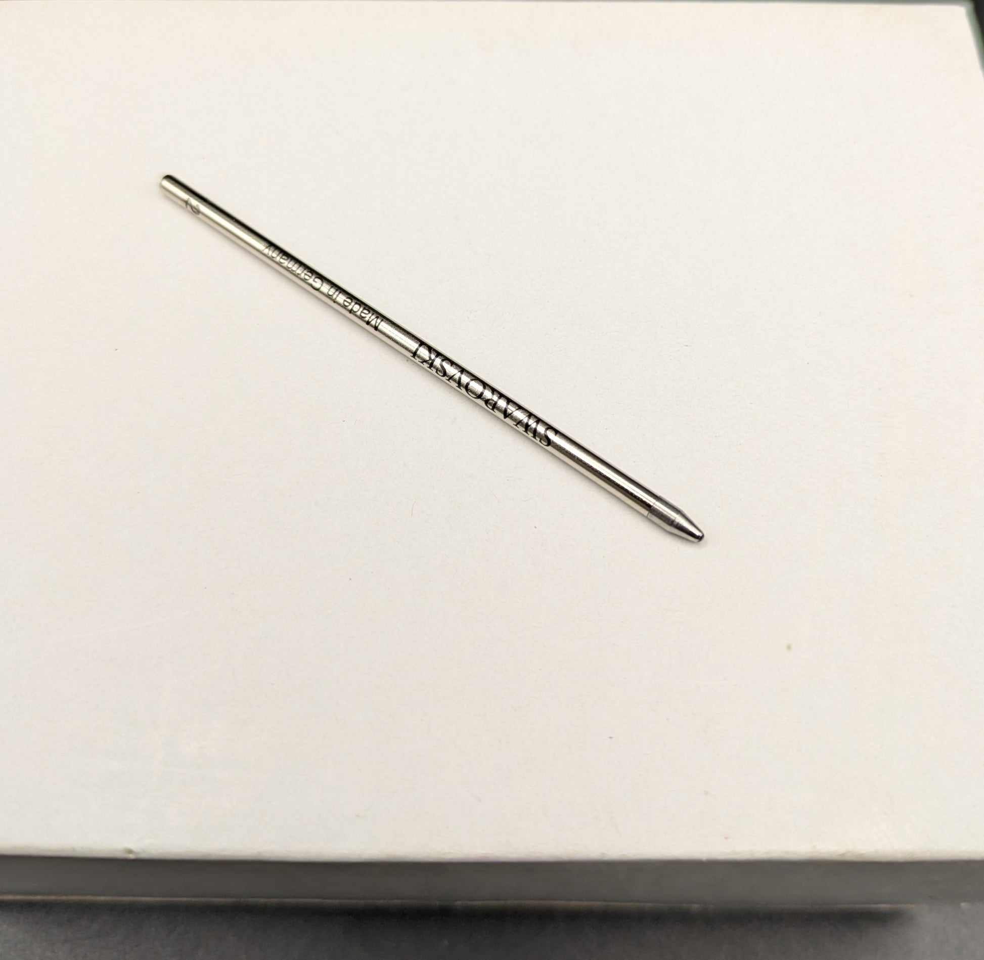 Metallic pen refill on a white surface with a black background