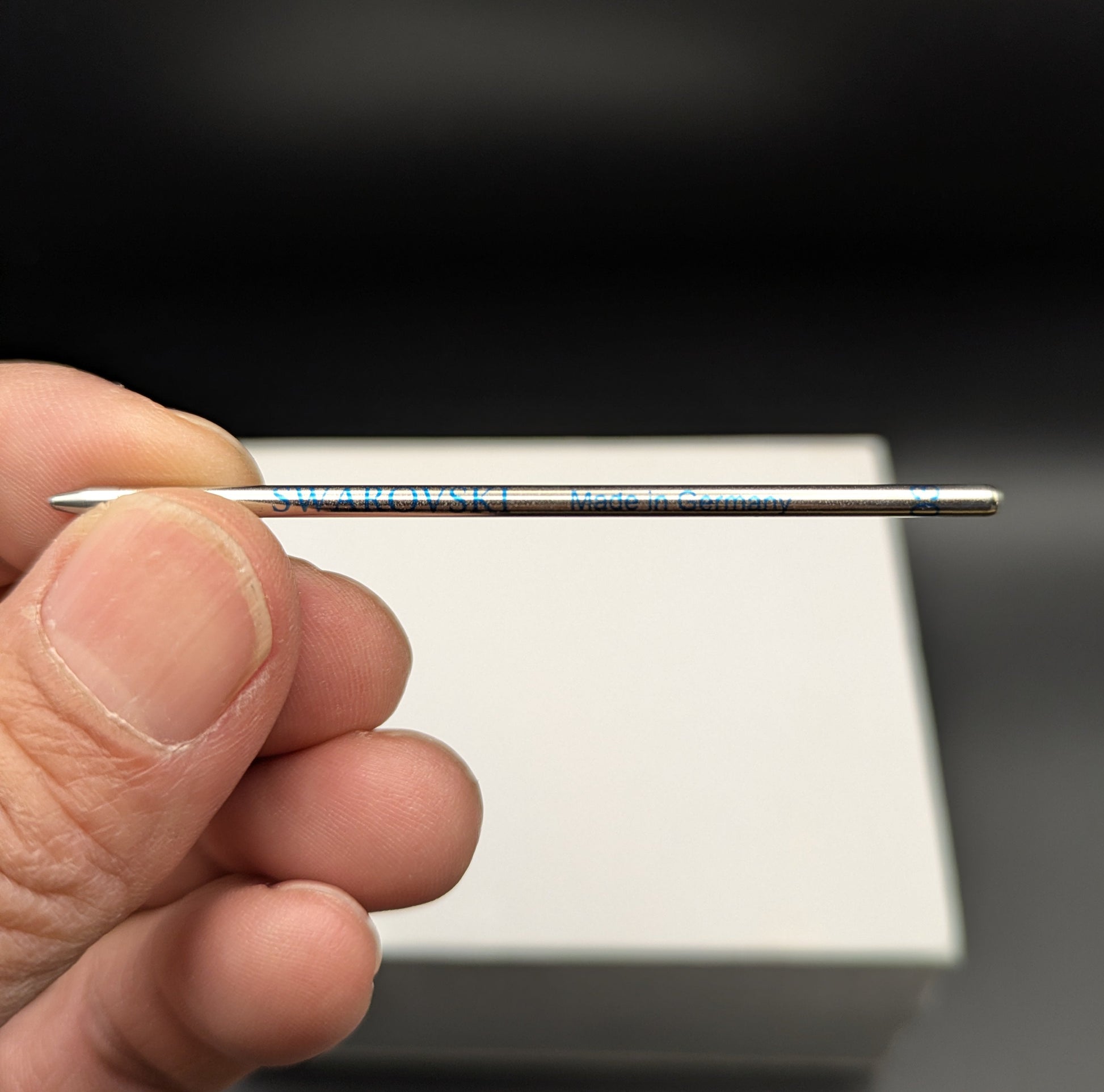 Hand holding a thin metal pen refill against a dark background