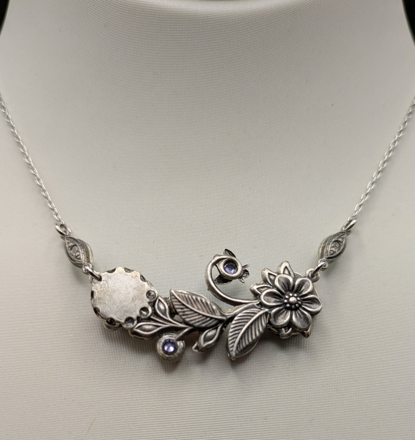 Silver necklace with floral and leaf designs on a mannequin.