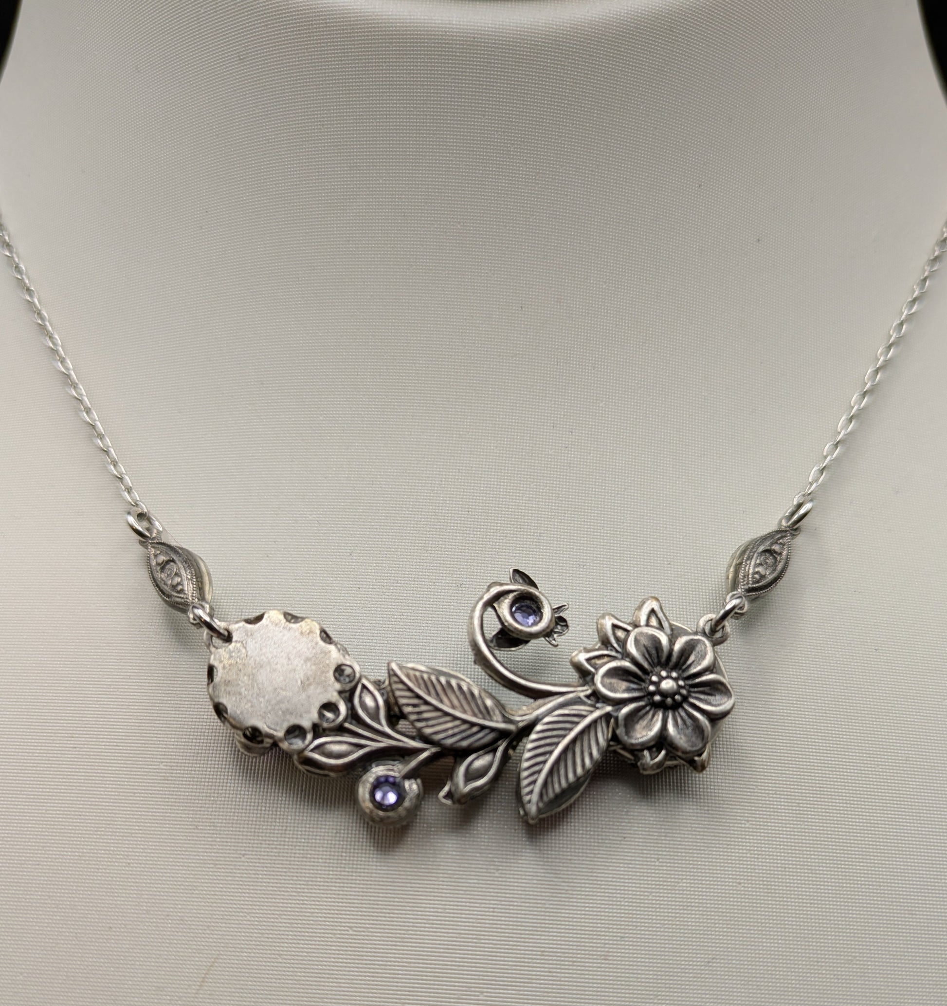 Silver necklace with floral and leaf designs on a mannequin.