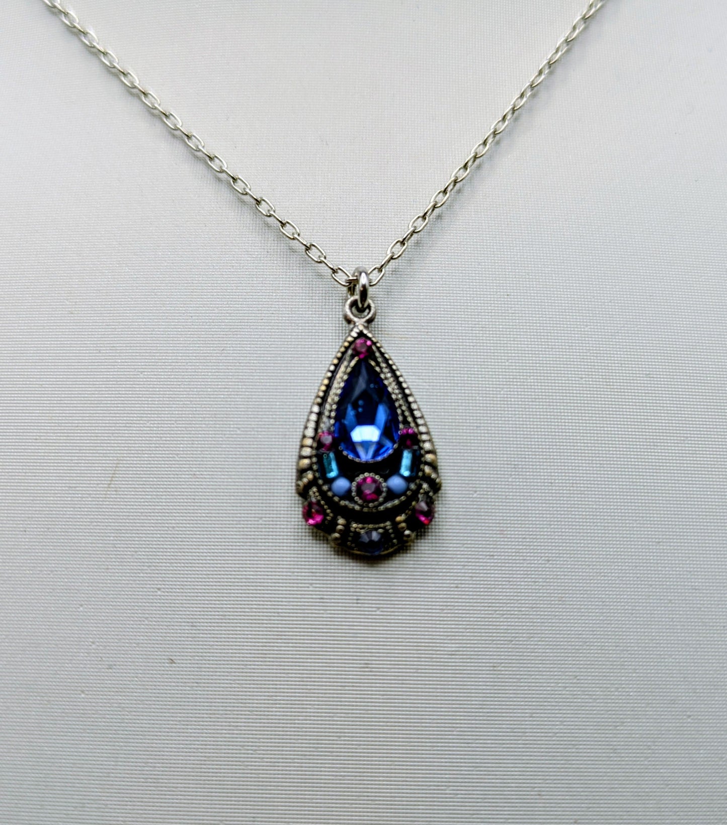 Teardrop-shaped pendant with colorful gemstones on a white background